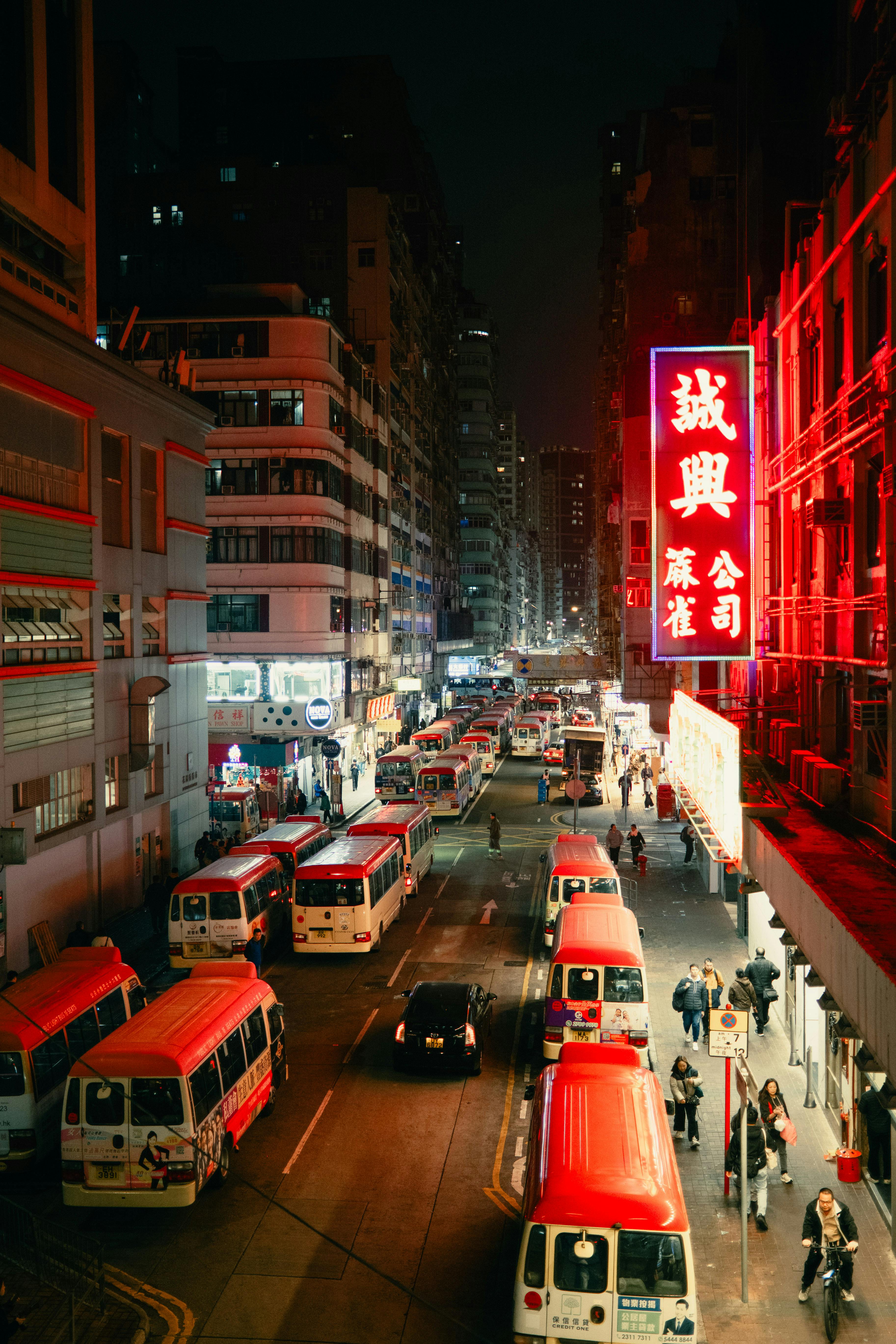 Kostenlos Eine urbane Nachtszene mit rot beleuchteten Schildern und Bussen auf einer belebten Straße fängt die pulsierende Energie Asiens ein. Stock-Foto