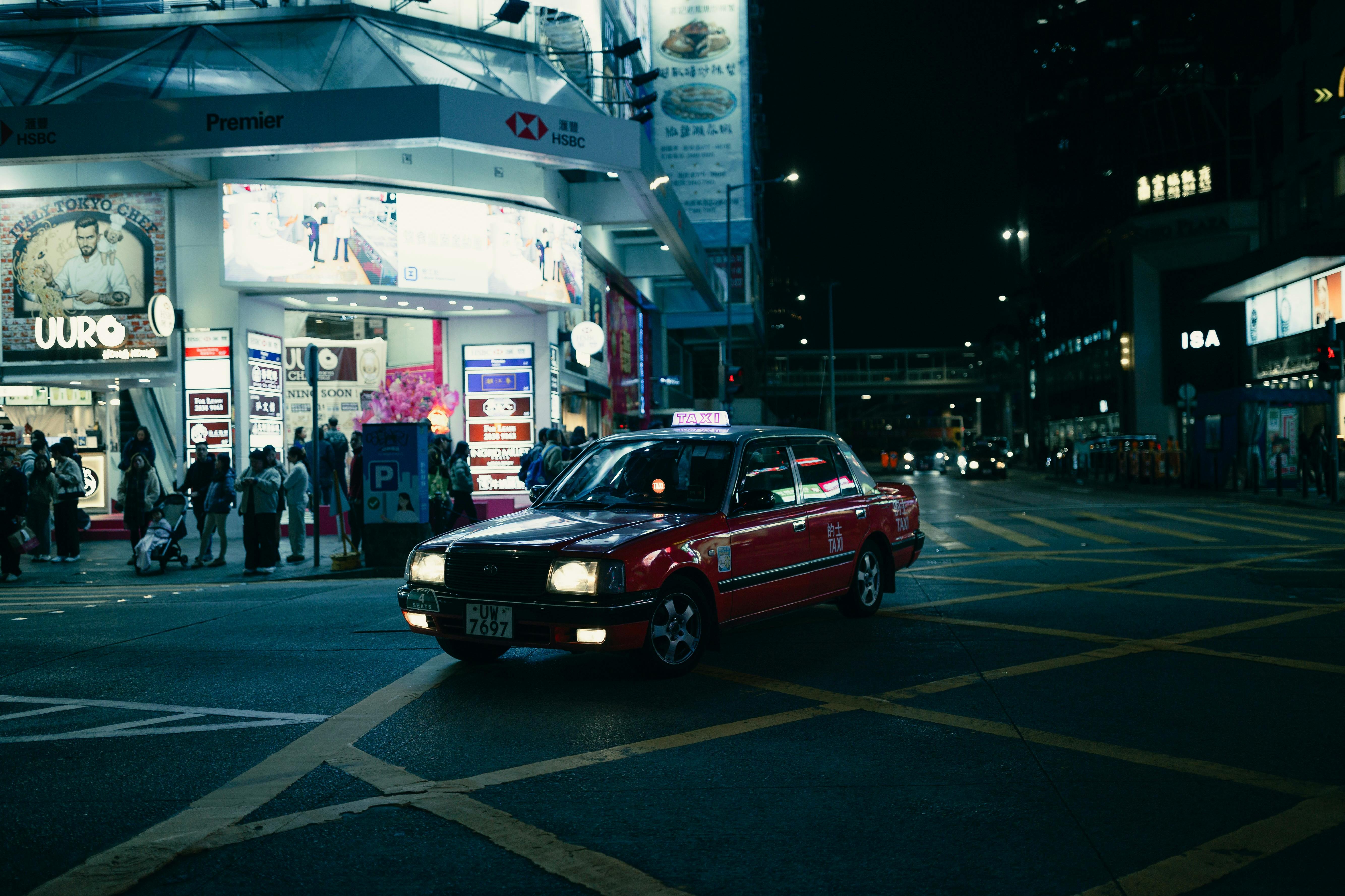 免费 一辆经典的红色出租车在霓虹灯闪烁的夜晚穿梭于香港熙熙攘攘的街道上。 素材图片