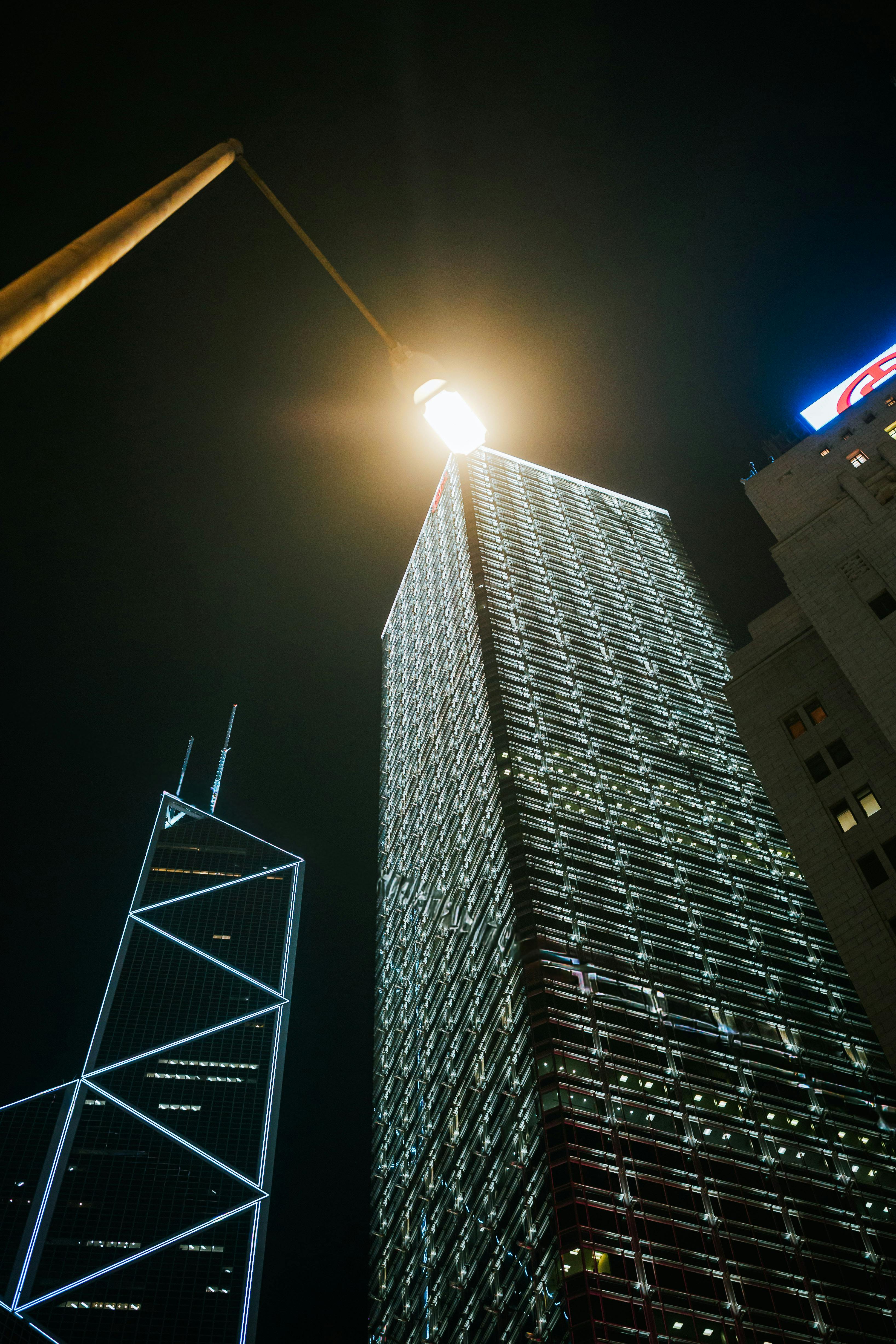 ingyenes Éjszakai látkép kivilágított felhőkarcolókról városi környezetben, erős utcai világítással. Stockfotó