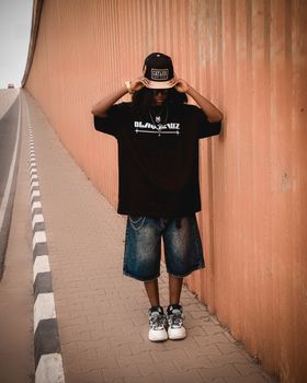 Young adult in casual streetwear poses confidently against urban backdrop.