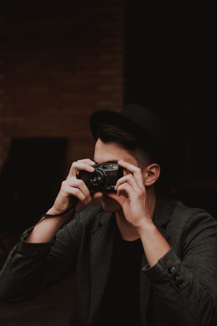 A fashionable young man taking photos with a vintage camera indoors.