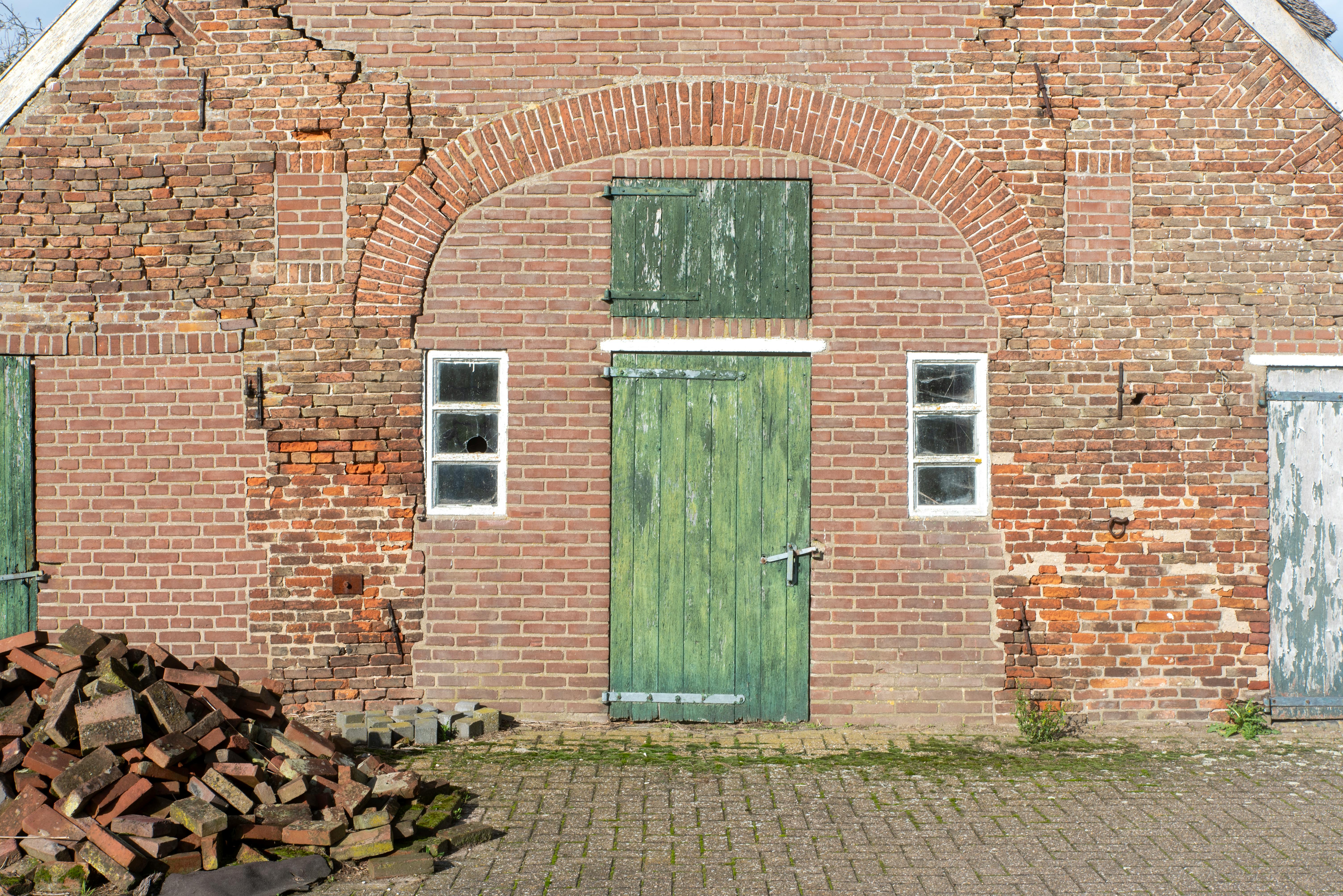 무료 햇빛 아래 녹색으로 칠해진 문과 갈라진 벽이 있는 낡은 벽돌 농가 건물. 스톡 사진