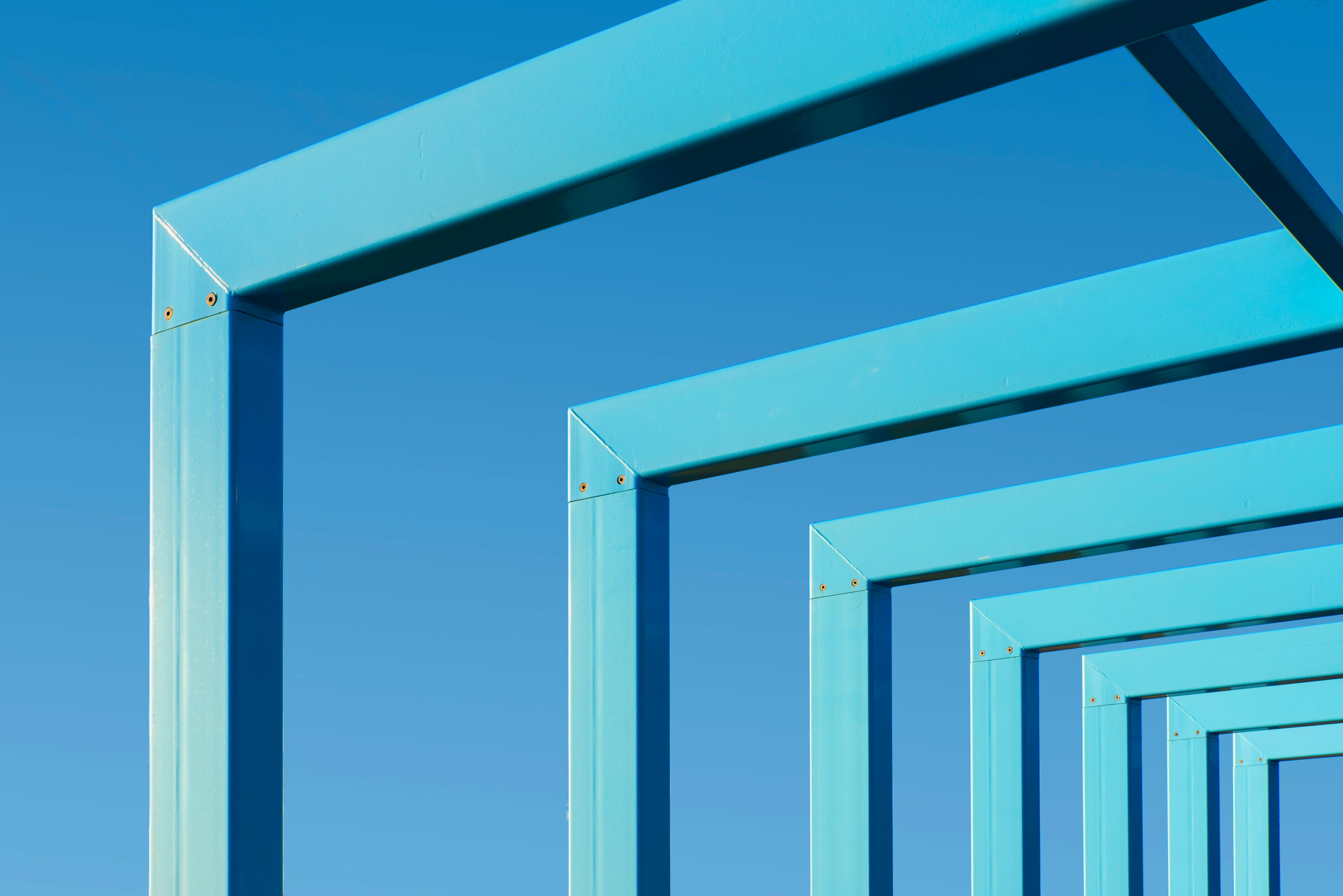 Gratis Vista astratta di cornici metalliche blu allineate contro un cielo blu intenso, creando un motivo geometrico. Foto a disposizione