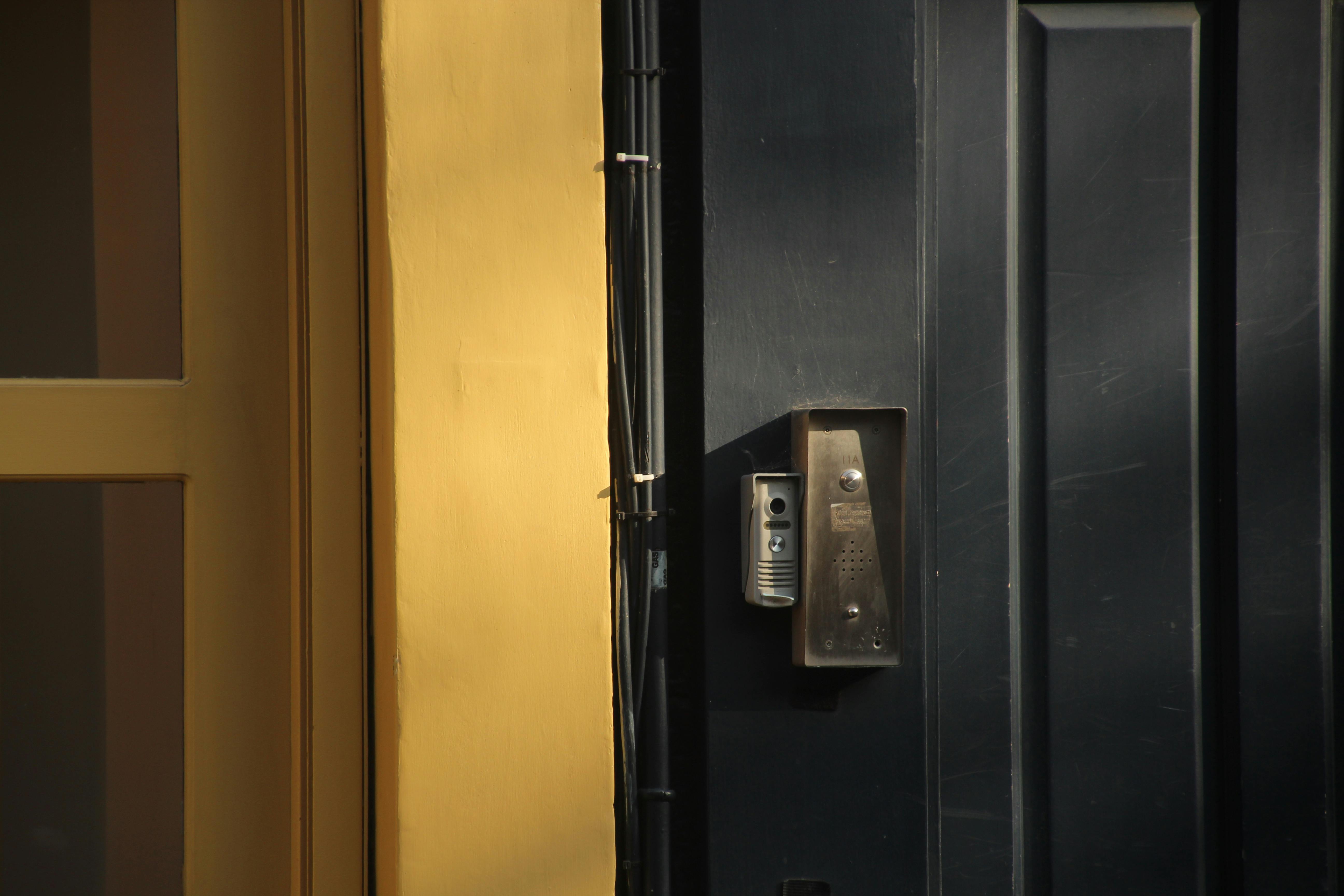 Free A close-up view of a dark door with a yellow frame and a metallic intercom system. Stock Photo