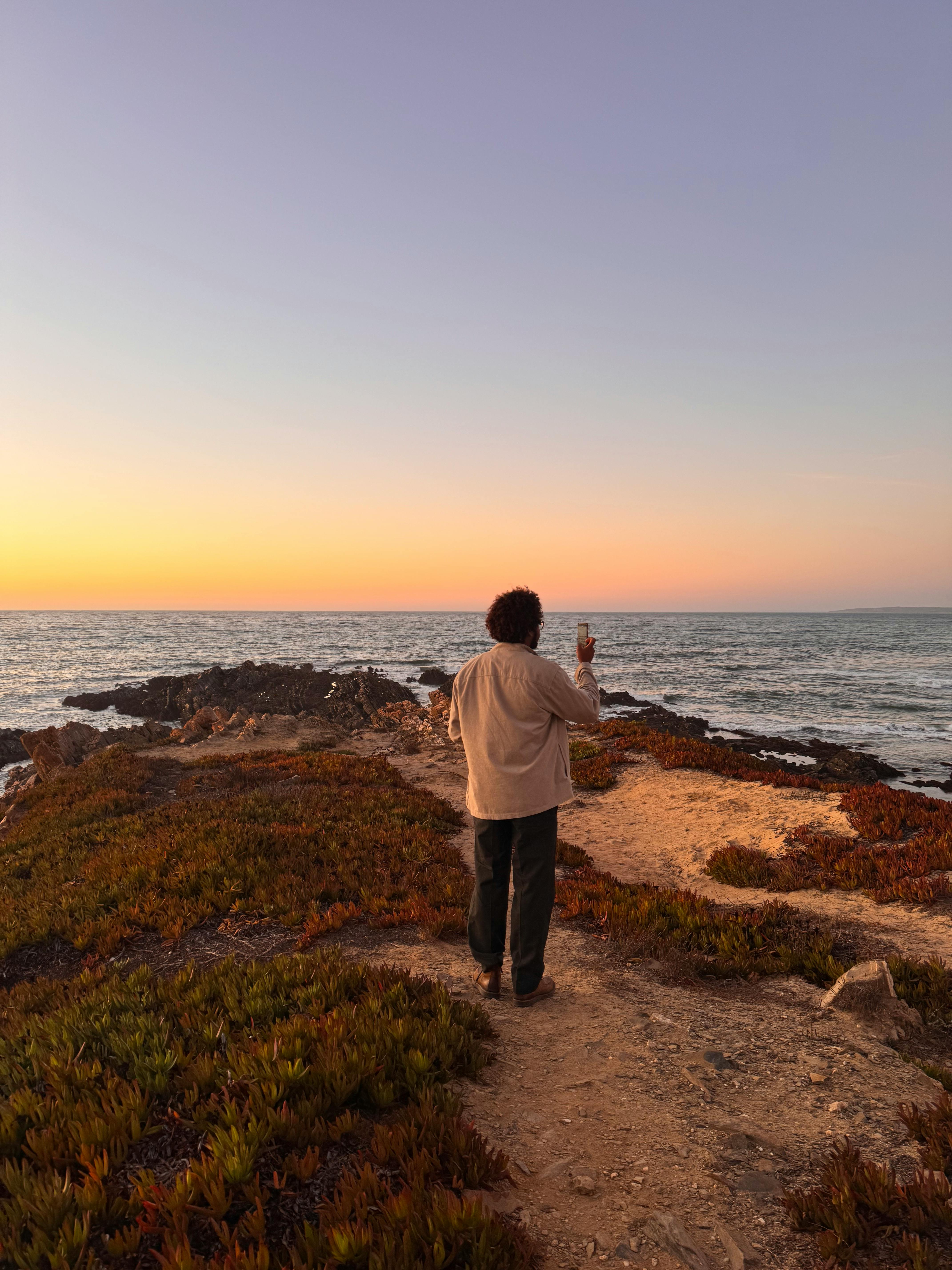 Δωρεάν Ένα άτομο φωτογραφίζει ένα εκπληκτικό ηλιοβασίλεμα πάνω από τον ωκεανό στην παραλία Aljezur στην Πορτογαλία. Φωτογραφία από στοκ φωτογραφιών