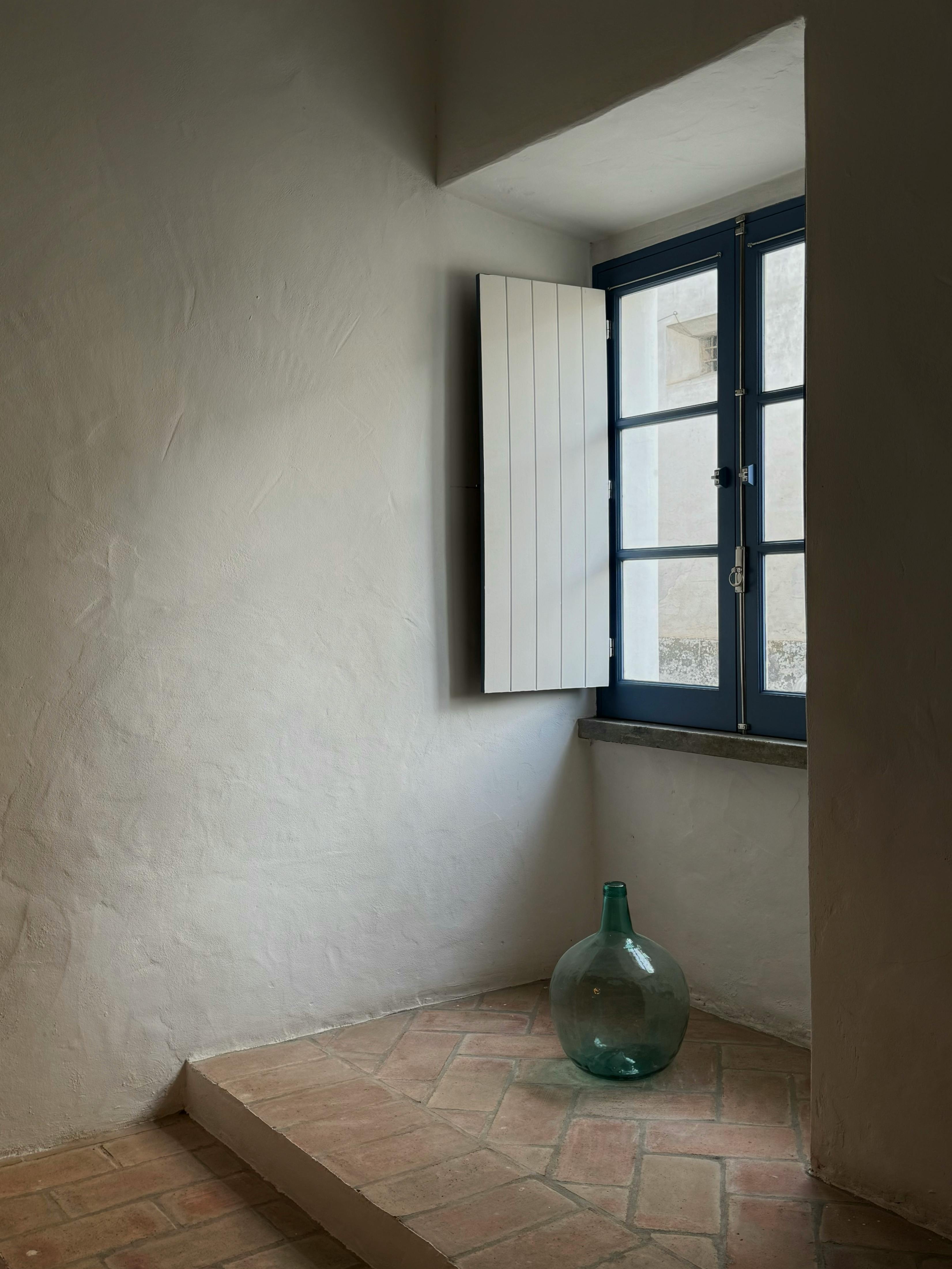 Kostnadsfria Minimalistisk rustik interiör med en vintage grön glaskanna på terrakottakakel vid ett blått fönster. Stock foto