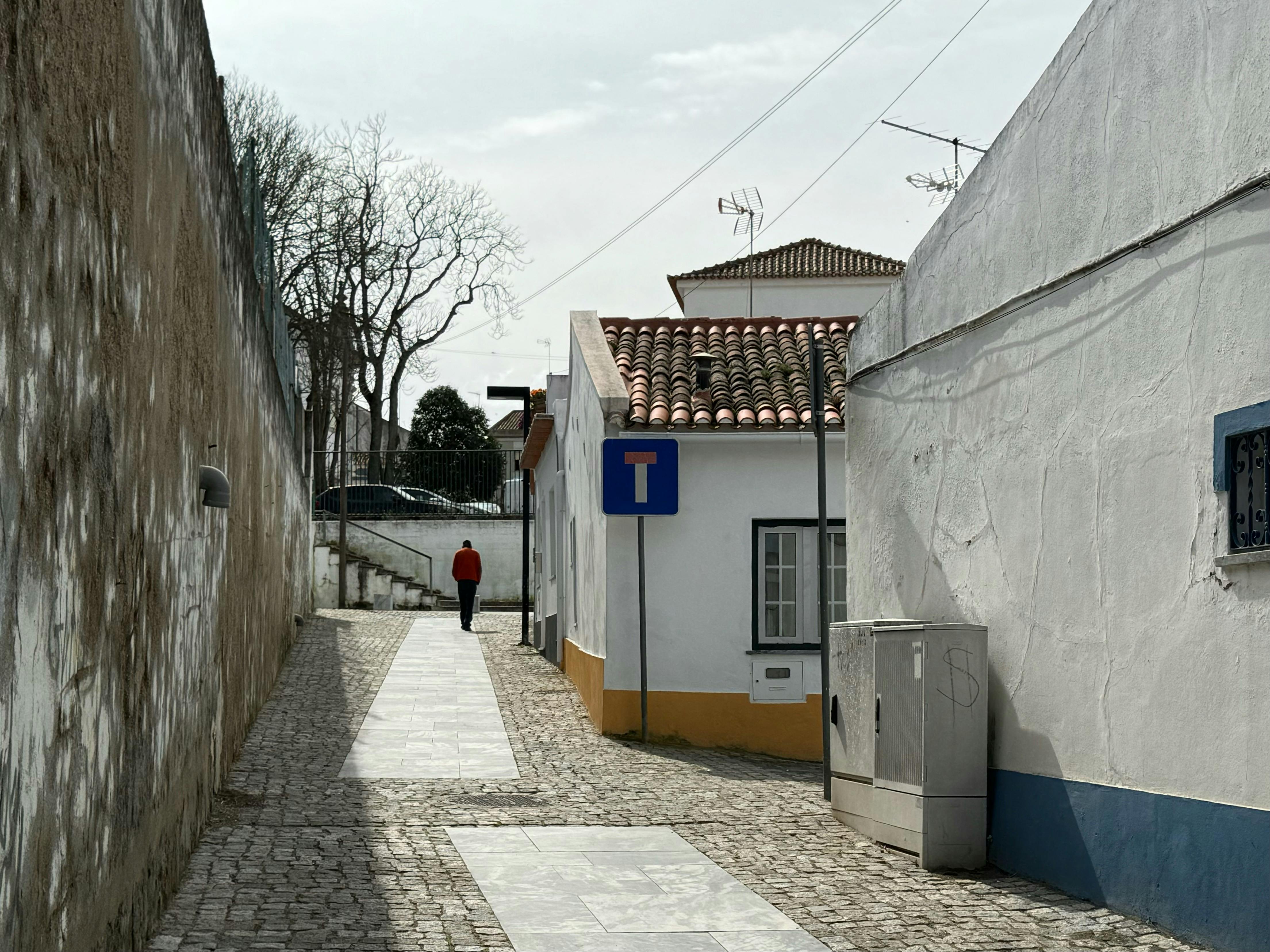 Δωρεάν Ένα γαλήνιο σοκάκι σε ένα πορτογαλικό χωριό με πλακόστρωτο μονοπάτι και πινακίδα σε σχήμα Τ. Φωτογραφία από στοκ φωτογραφιών