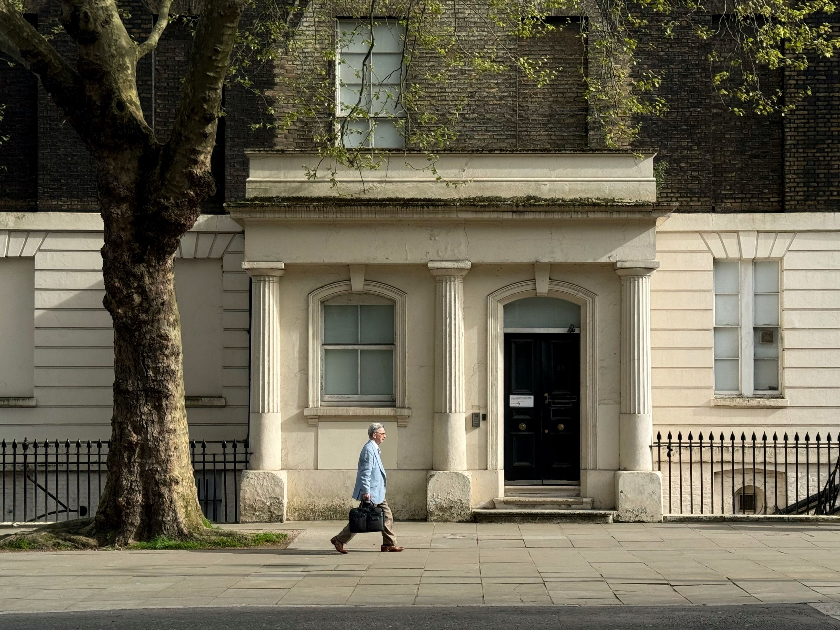 A man walks past a historic building facade in a city street, showcasing classic architectural elements.