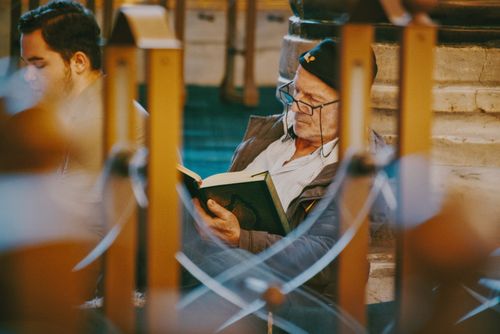 Free Senior man with glasses reading a book indoors with a focused expression. Stock Photo