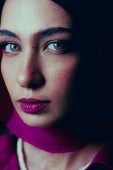Close-up portrait of a woman wearing a magenta scarf and intense look, captured indoors.
