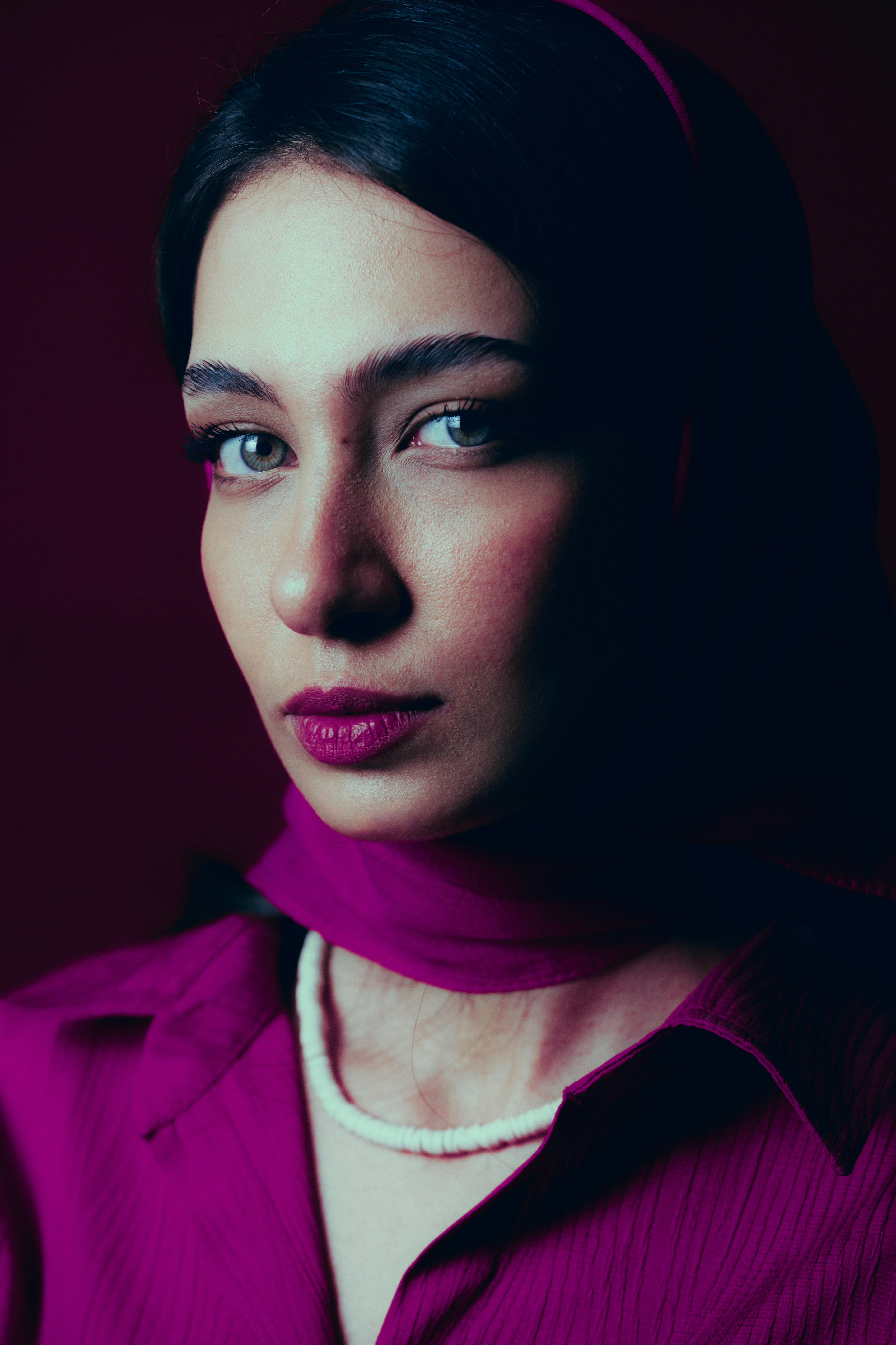 Gratis Suggestivo ritratto di una donna che indossa un hijab e un top viola, immortalato con un'illuminazione spettacolare. Foto a disposizione