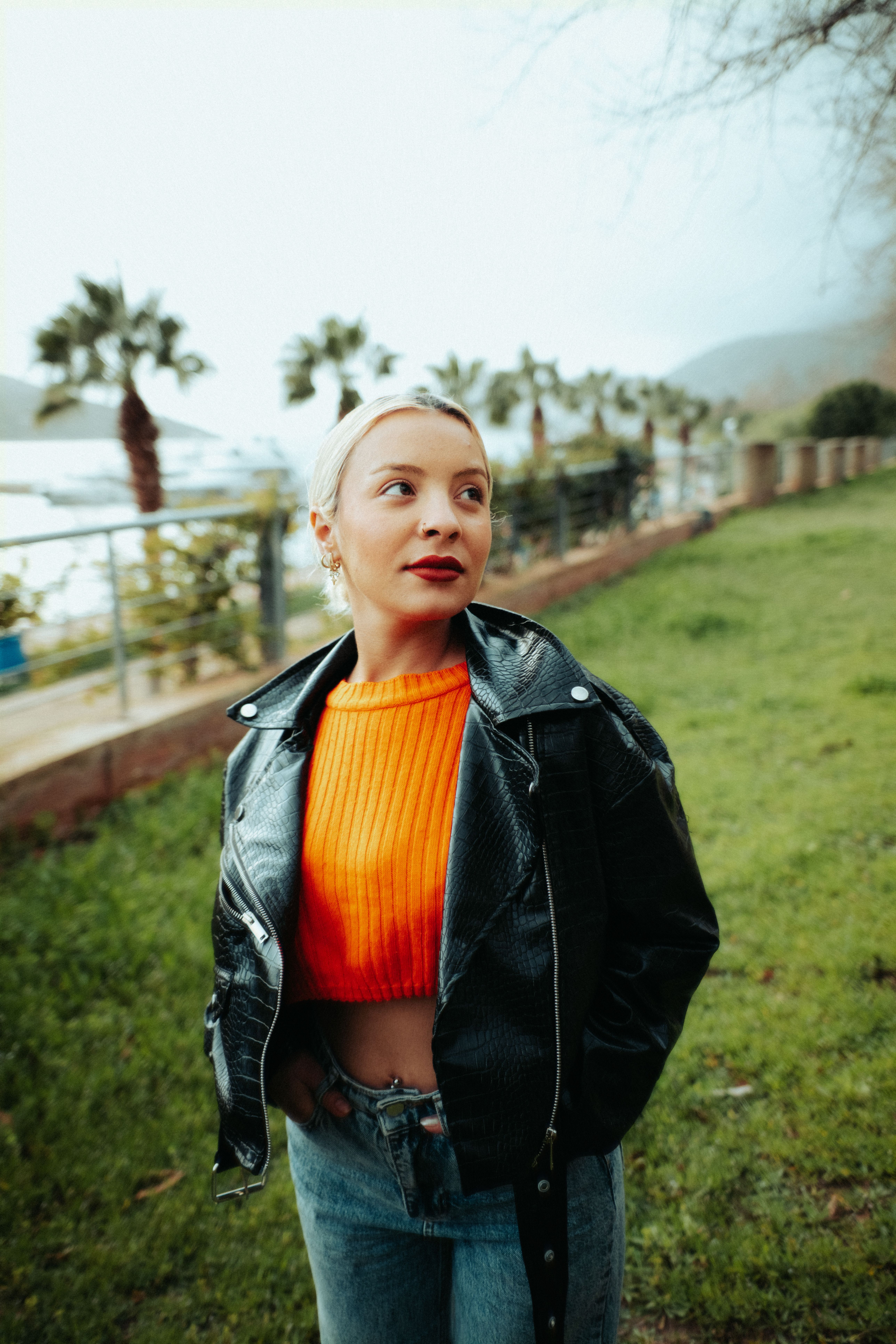 Fashionable woman in orange sweater and black leather jacket in a park setting.
