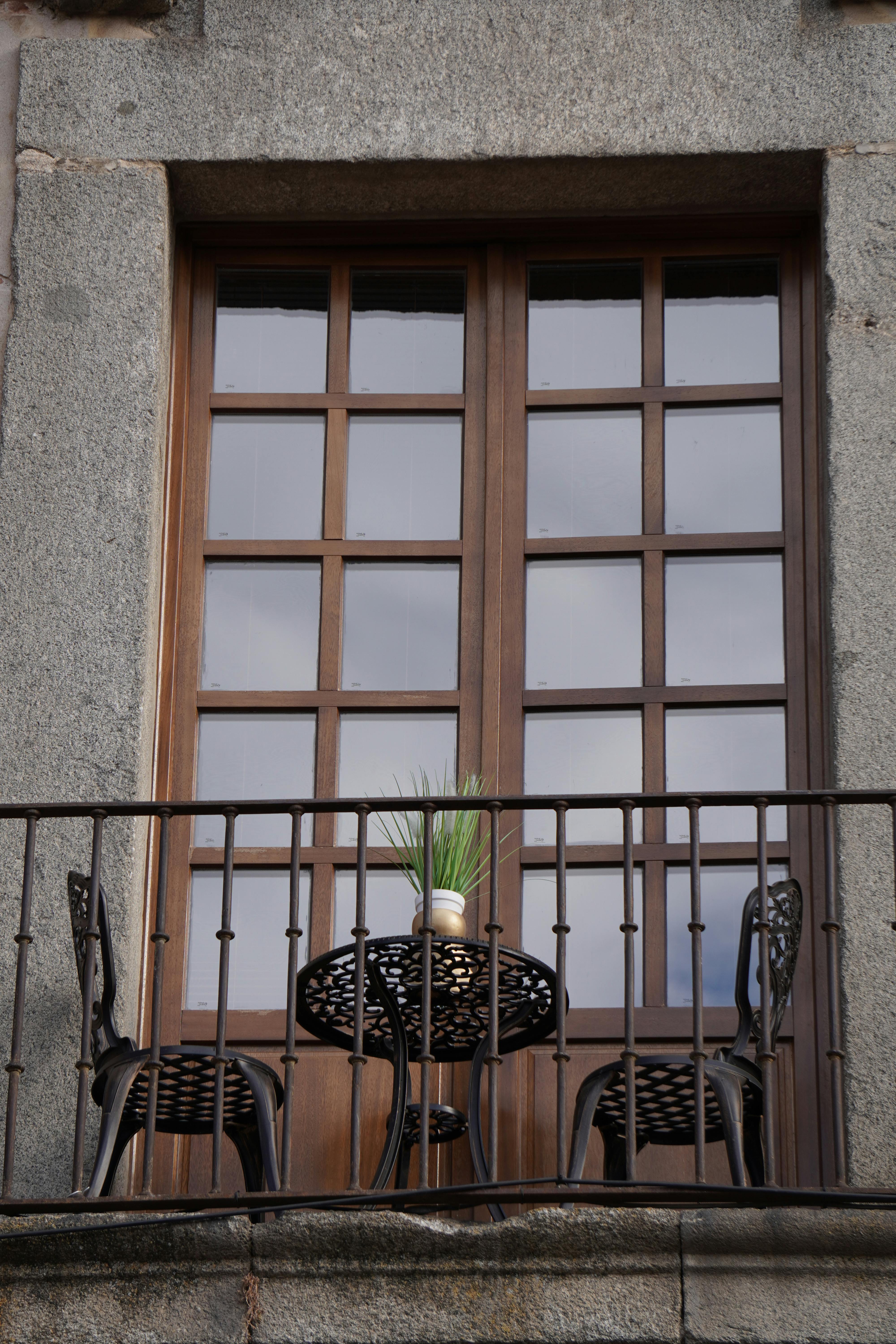 Gratis Elegant stenbalkon med jernmøbler og potteplante, der afspejler klassisk arkitekturstil. Lagerfoto