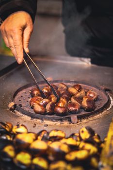Hand roasting chestnuts on outdoor grill, perfect for fall street food themes.