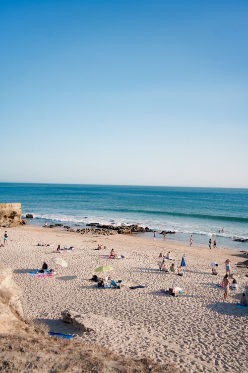 Free Relaxing beach scene with people enjoying a sunny day by the ocean, perfect for summer vacation themes. Stock Photo