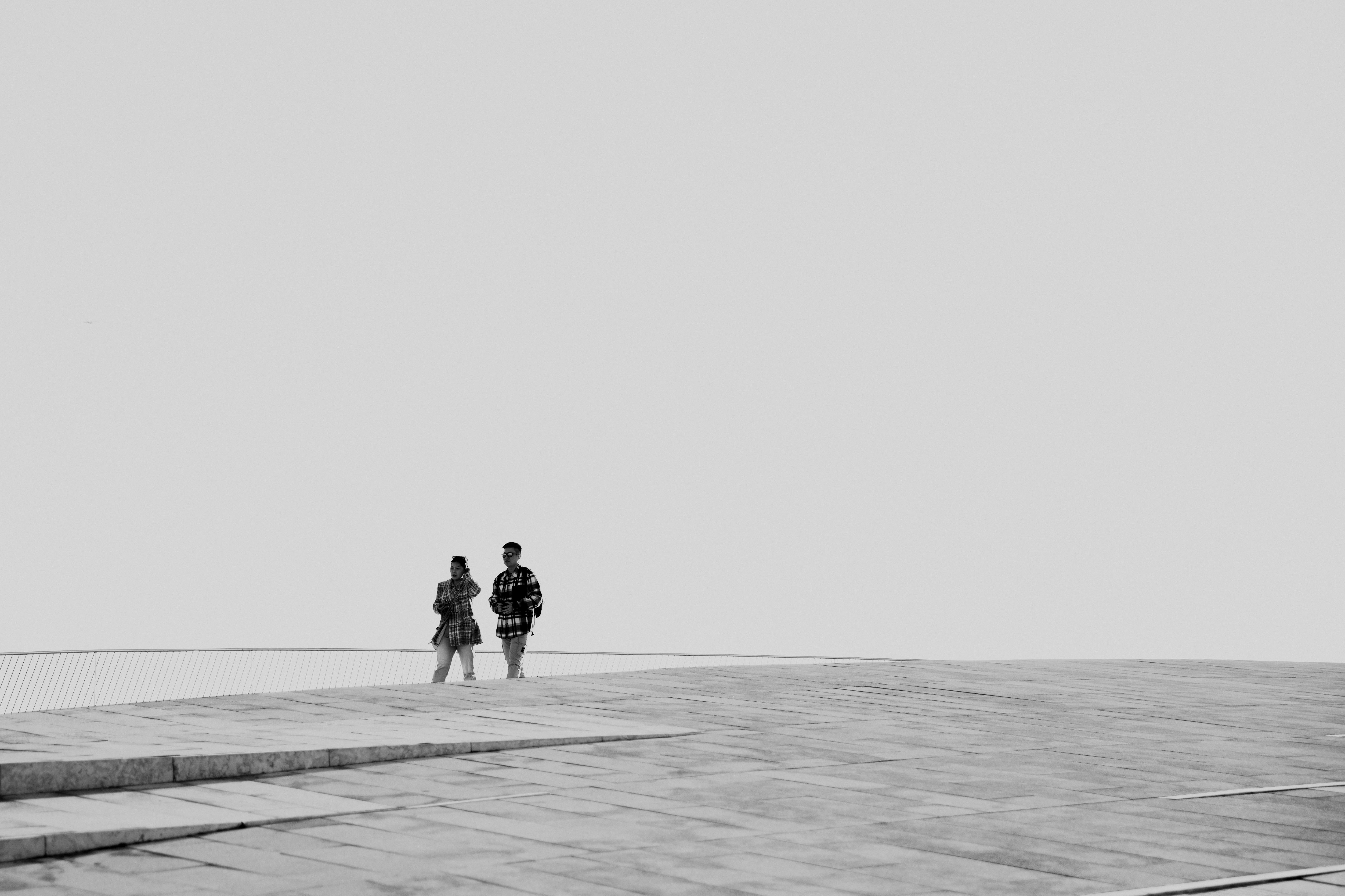Free Two people walking on a modern architectural structure under a clear sky. Stock Photo