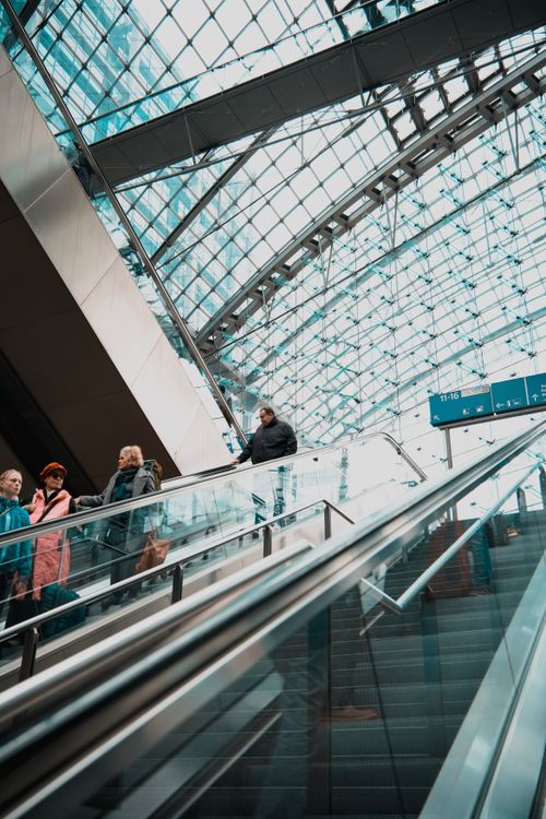 Free Travelers on an escalator in a modern building with a geometric glass ceiling. Stock Photo