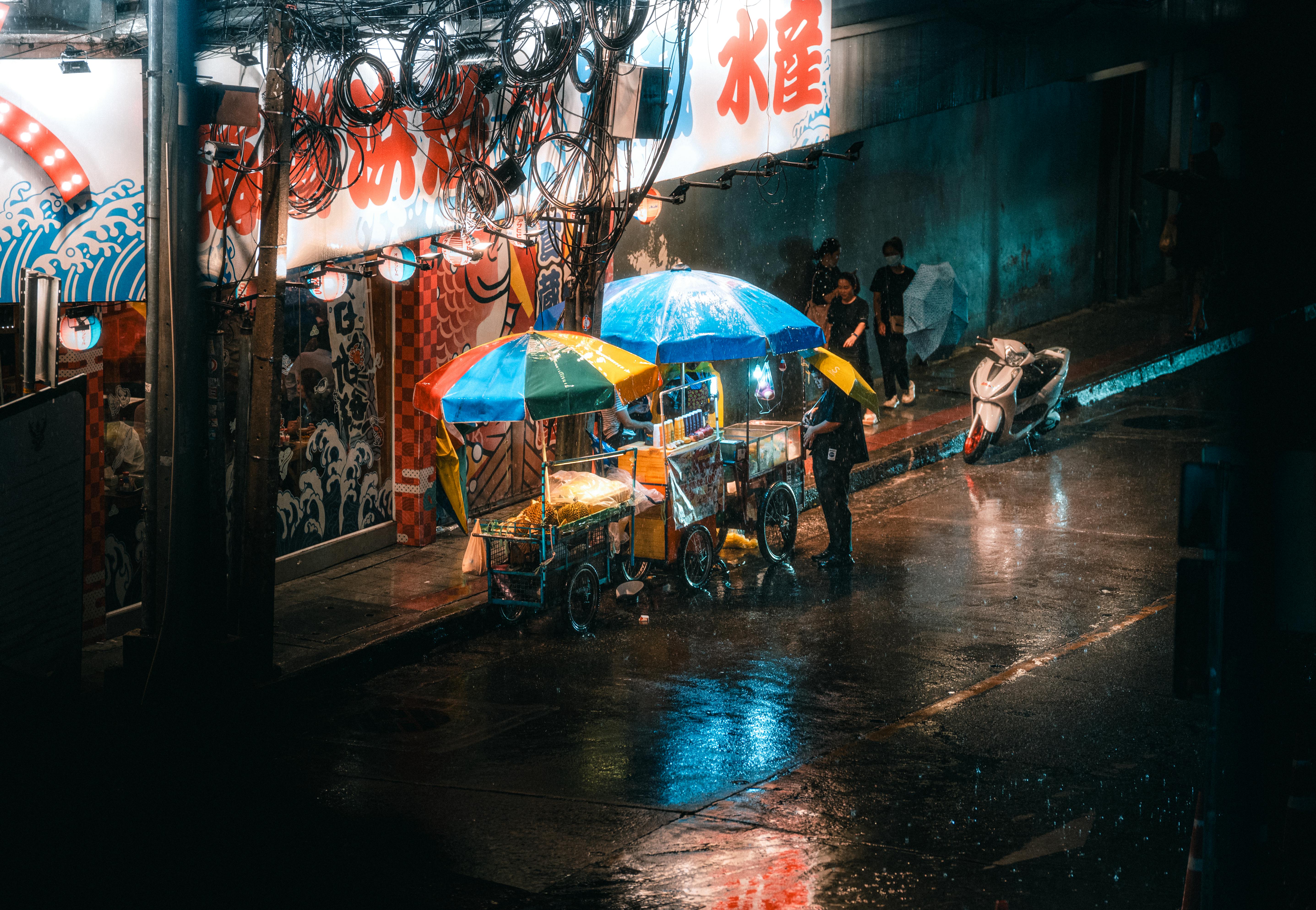 Ücretsiz Yağmurlu Bangkok gece pazarındaki rengarenk sokak yemek arabaları. Stok Fotoğraflar