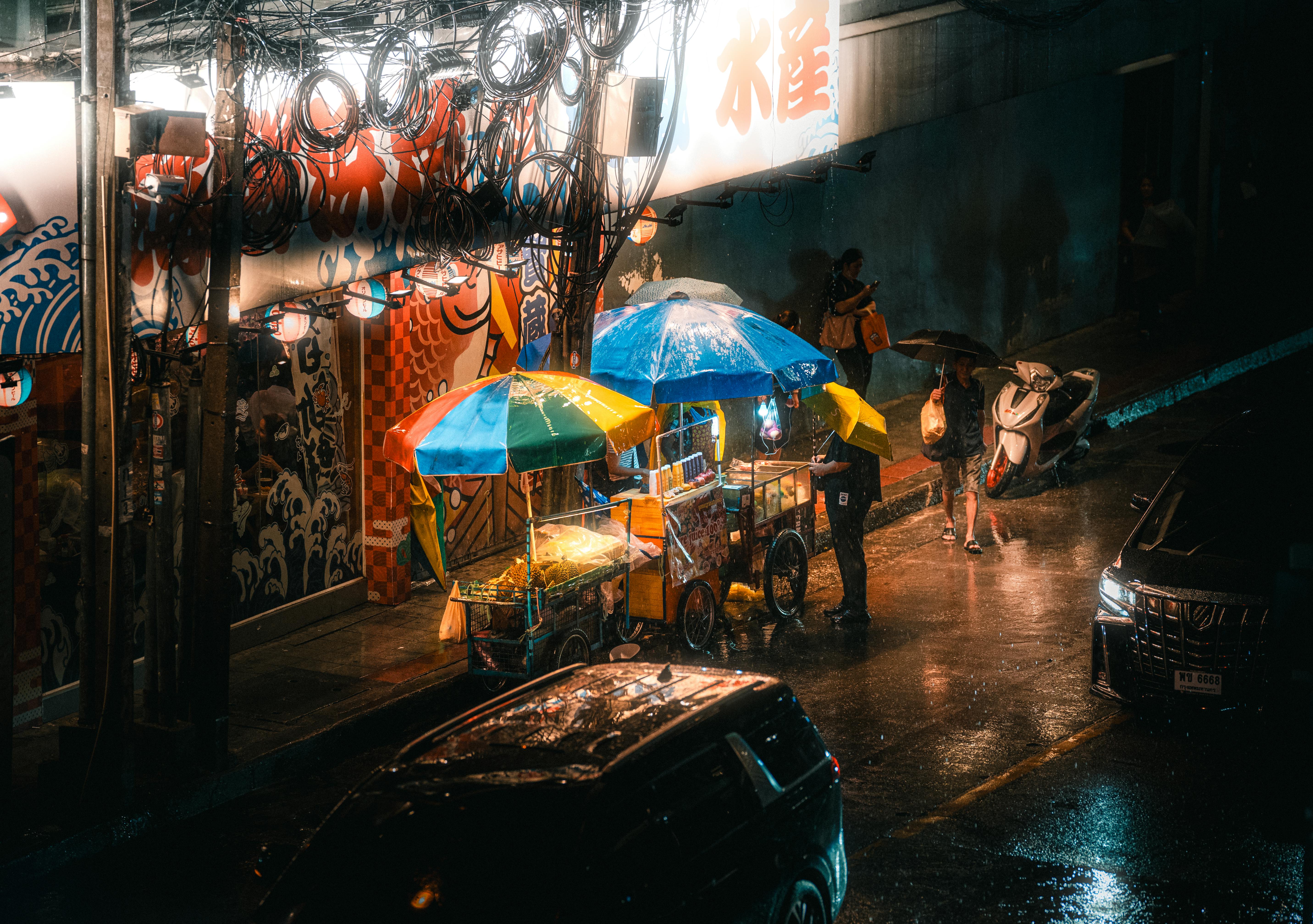 Ücretsiz Gece vakti yağmurlu Bangkok'ta rengarenk şemsiyelerin altında hareketli sokak yemek tezgahları. Stok Fotoğraflar