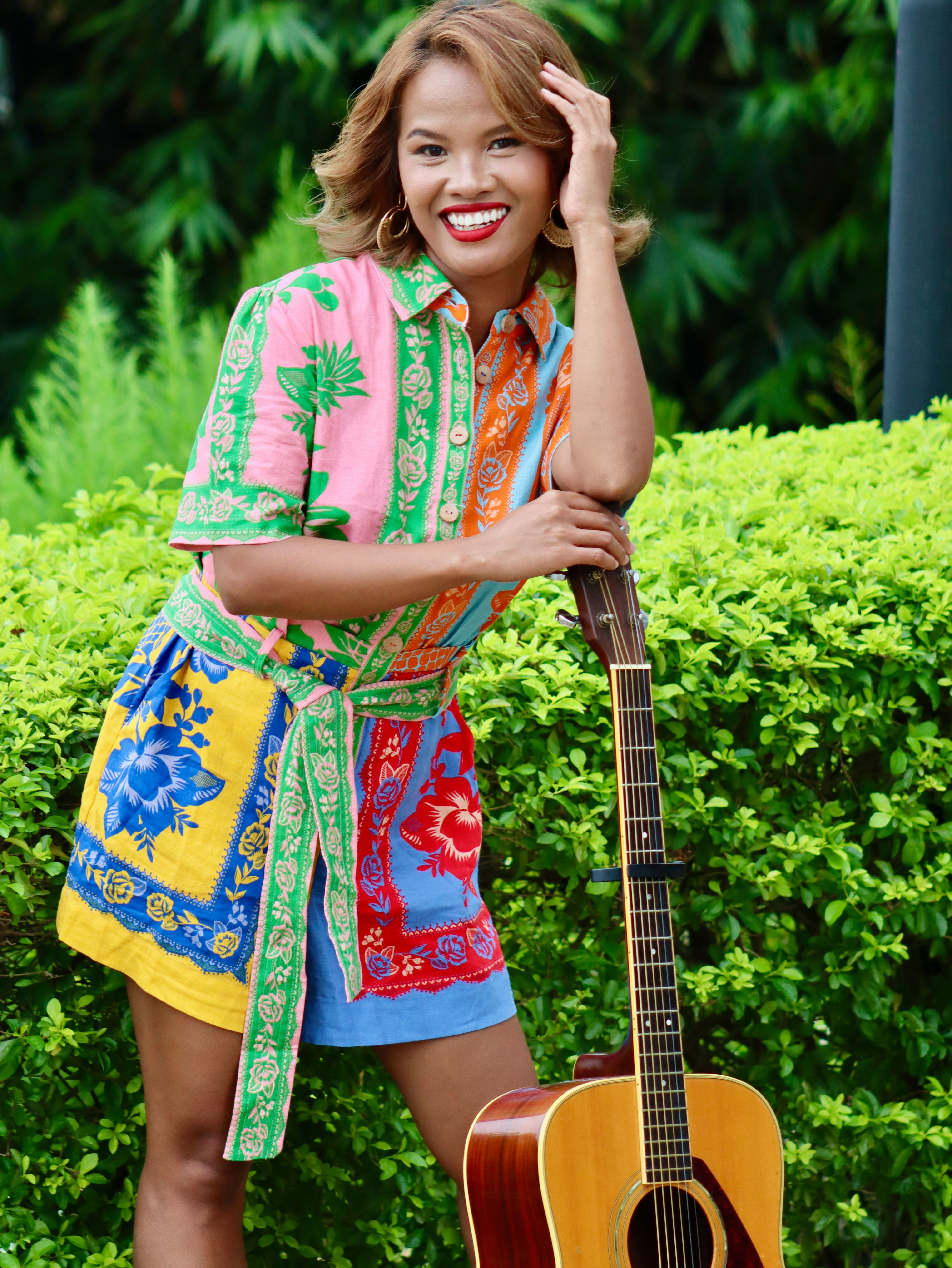 Joyful Filipino woman in colorful outfit posing with guitar outdoors in Eastern Visayas.