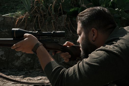 Focused man in outdoor setting aiming rifle with scope for precision shooting.