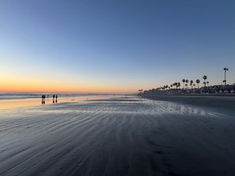 A tranquil twilight scene at Oceanside Beach, showcasing a vibrant sunset and palm tree silhouettes.