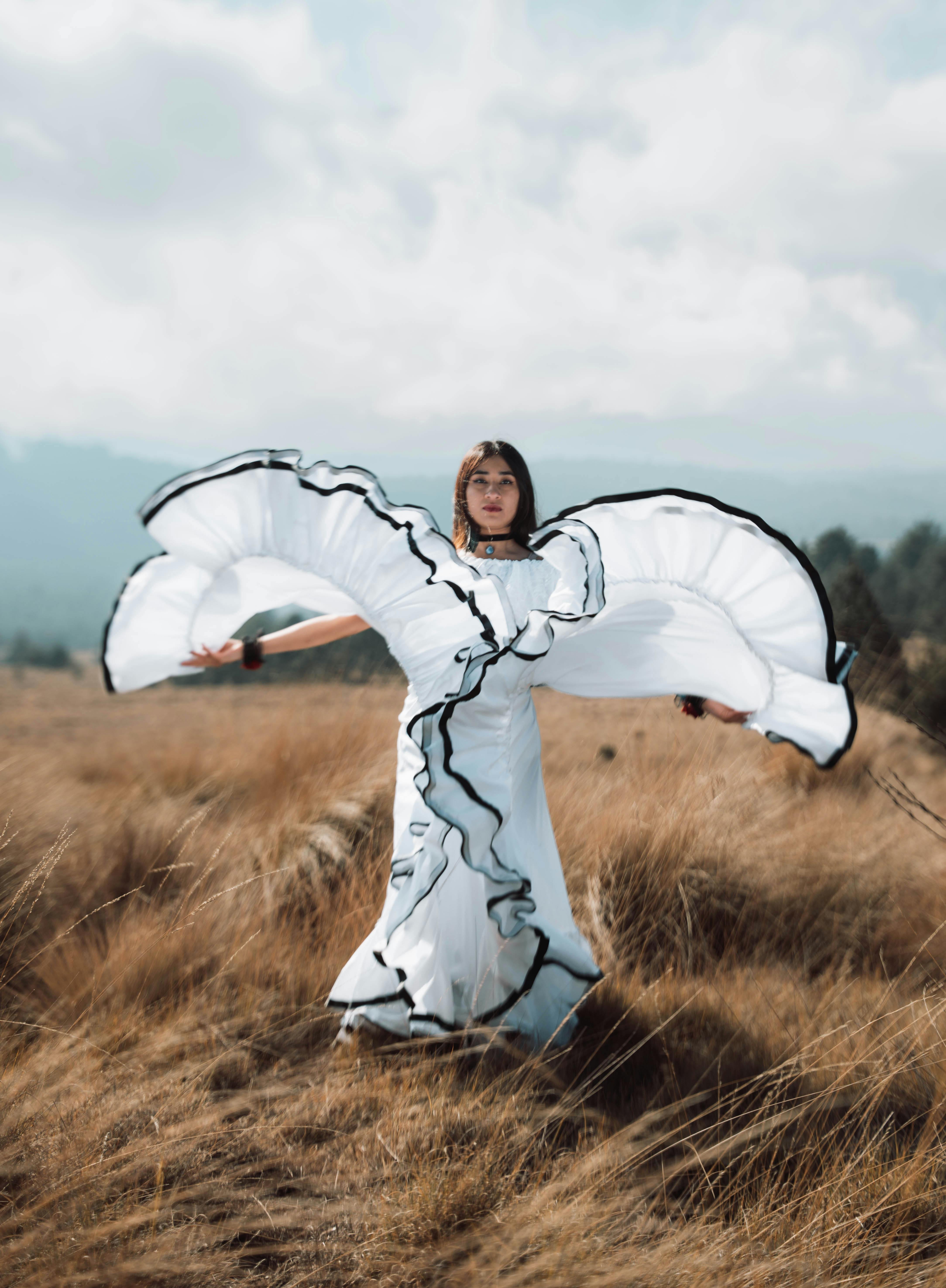 ฟรี หญิงสาวคนหนึ่งกำลังเต้นรำอย่างงดงามในทุ่งโล่ง ชุดสีขาวของเธอพลิ้วไหวไปตามสายลม คลังภาพถ่าย