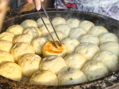 An artistic close-up of fried dumplings being cooked in a large pan outdoors.