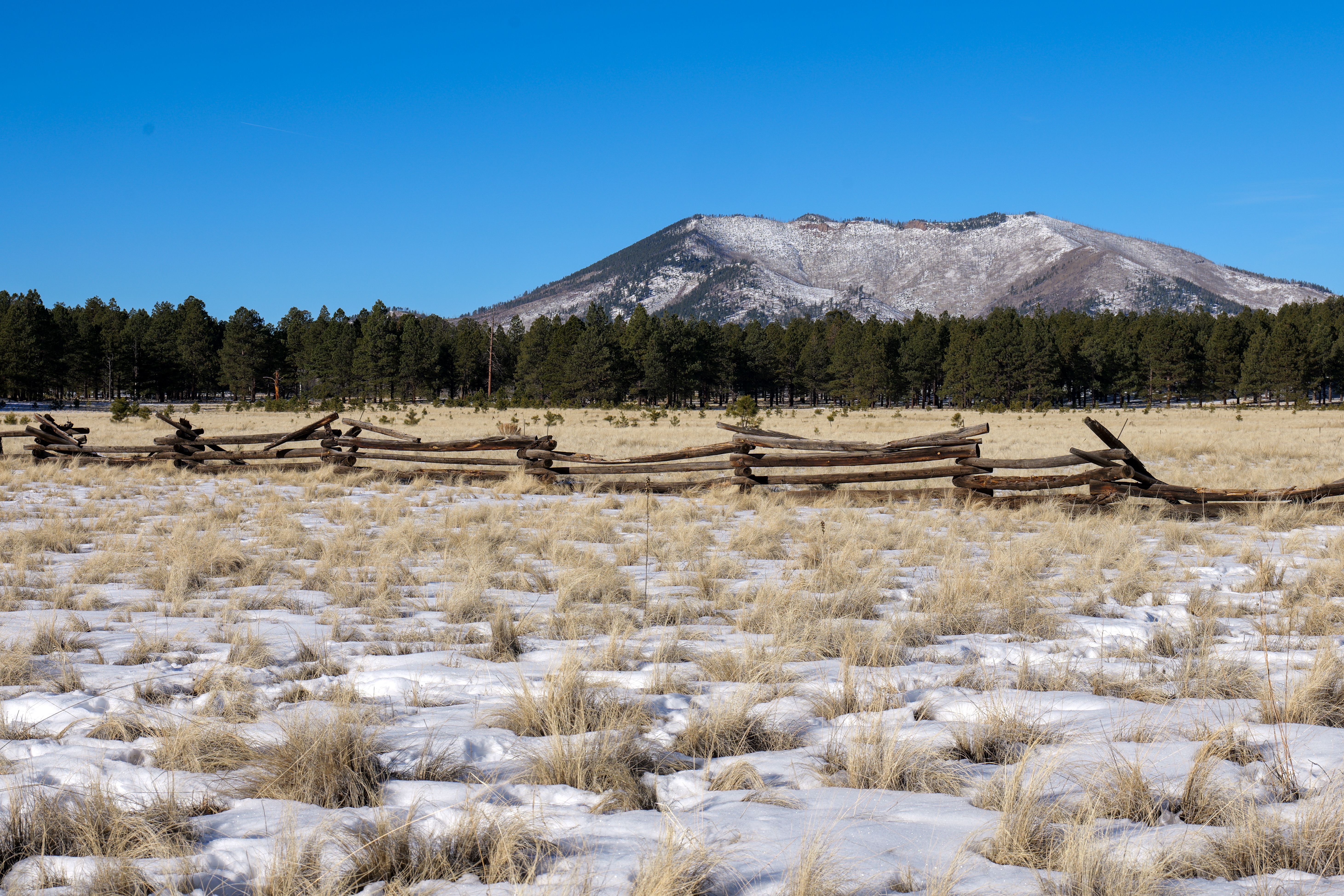 A scenic view of a snow-dusted landscape, wooden fence, and distant mountains under a clear blue sky in Phoenix, Arizona.
