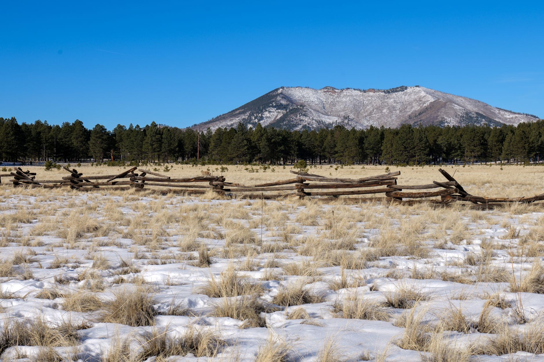 A scenic view of a snow-dusted landscape, wooden fence, and distant mountains under a clear blue sky in Phoenix, Arizona.