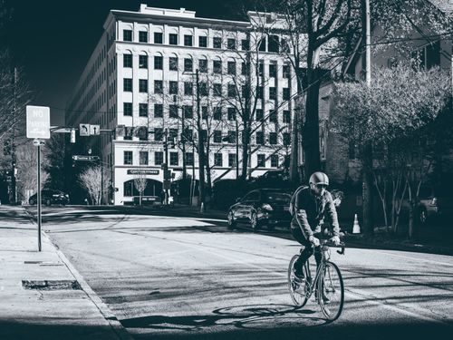Free A cyclist wearing a helmet rides a bicycle along a city street near a large building. Stock Photo