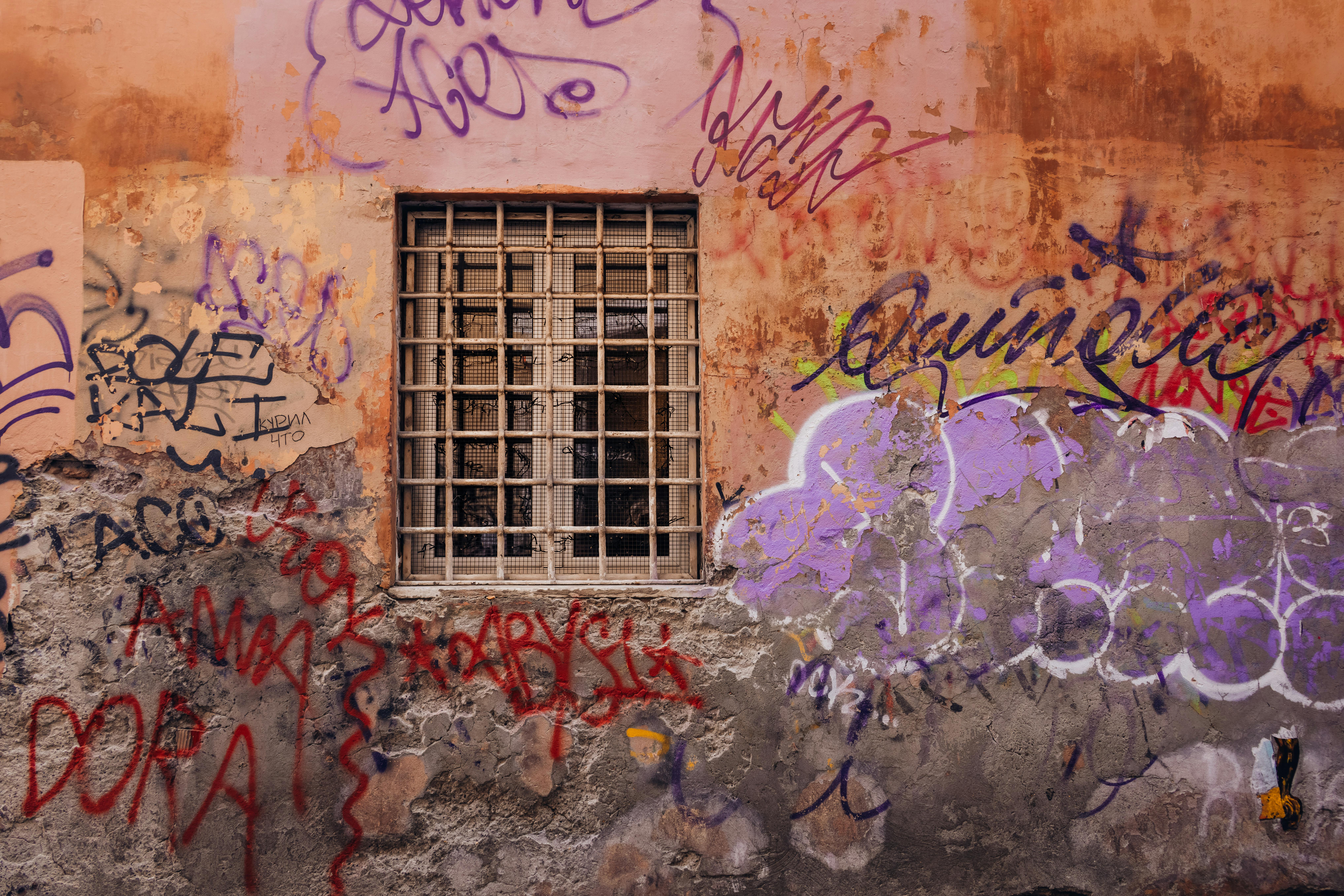 Free Vibrant graffiti art on an aged urban wall featuring a barred window, showcasing street art creativity. Stock Photo