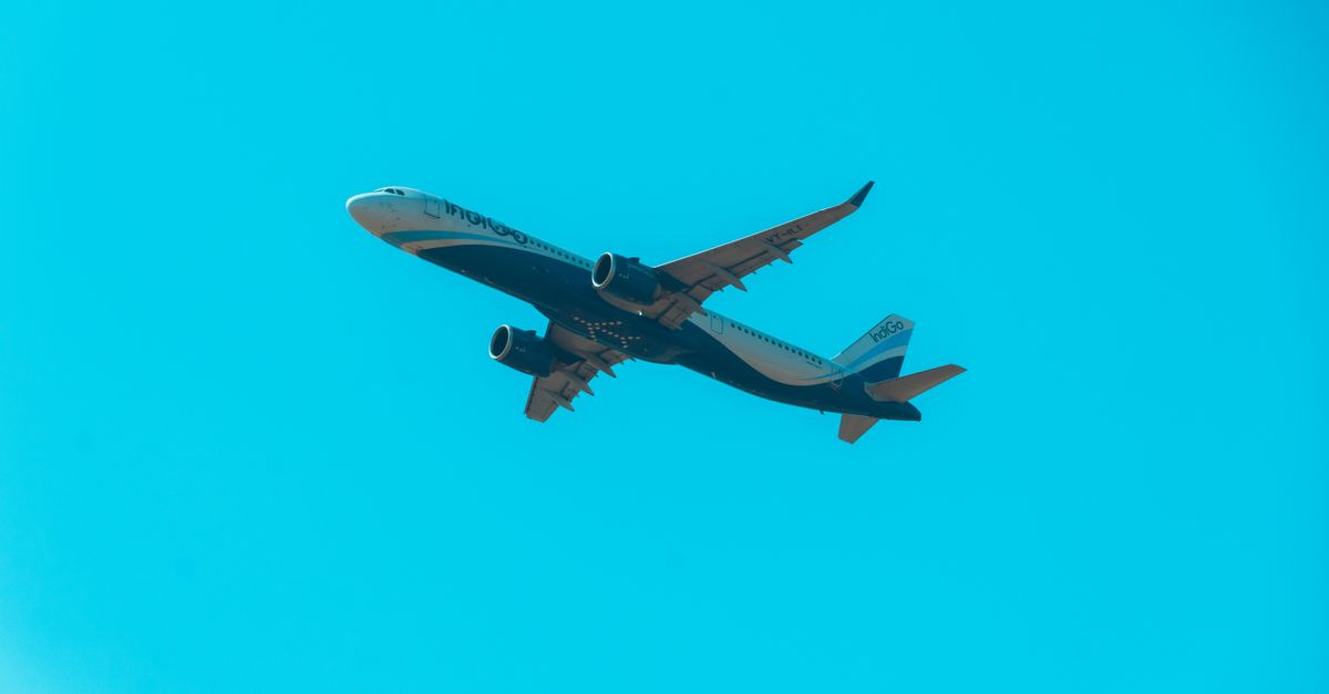 An Etihad passenger jet and an IndiGo aircraft park at an airport gate under a clear blue sky.