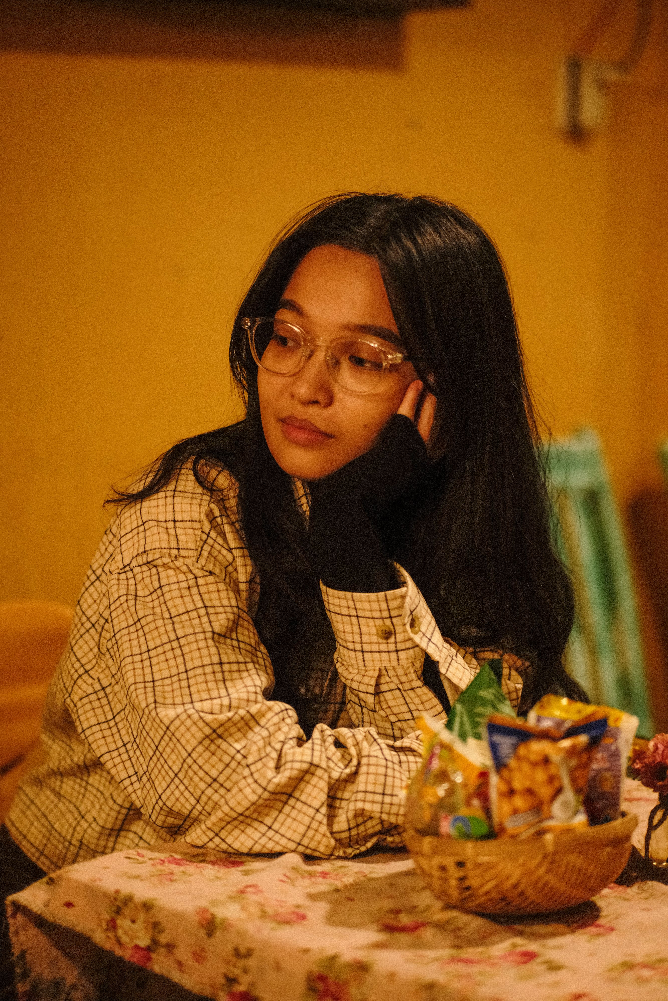A woman with glasses in a casual cozy setting, enjoying snacks in a warm-toned Hội An café.