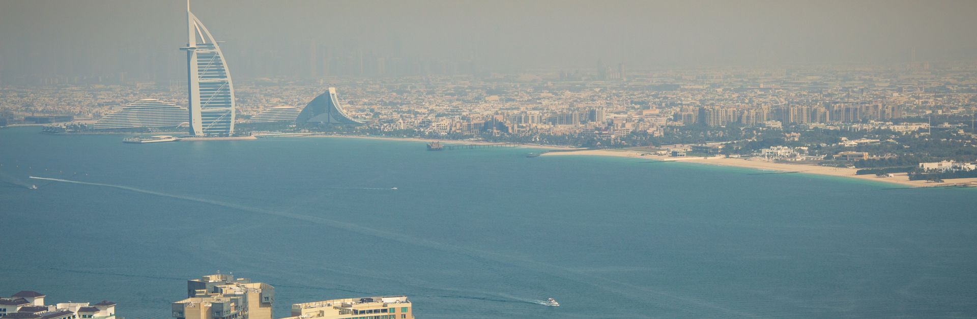 A breathtaking aerial view of the Dubai skyline featuring the iconic Burj Al Arab and pristine water