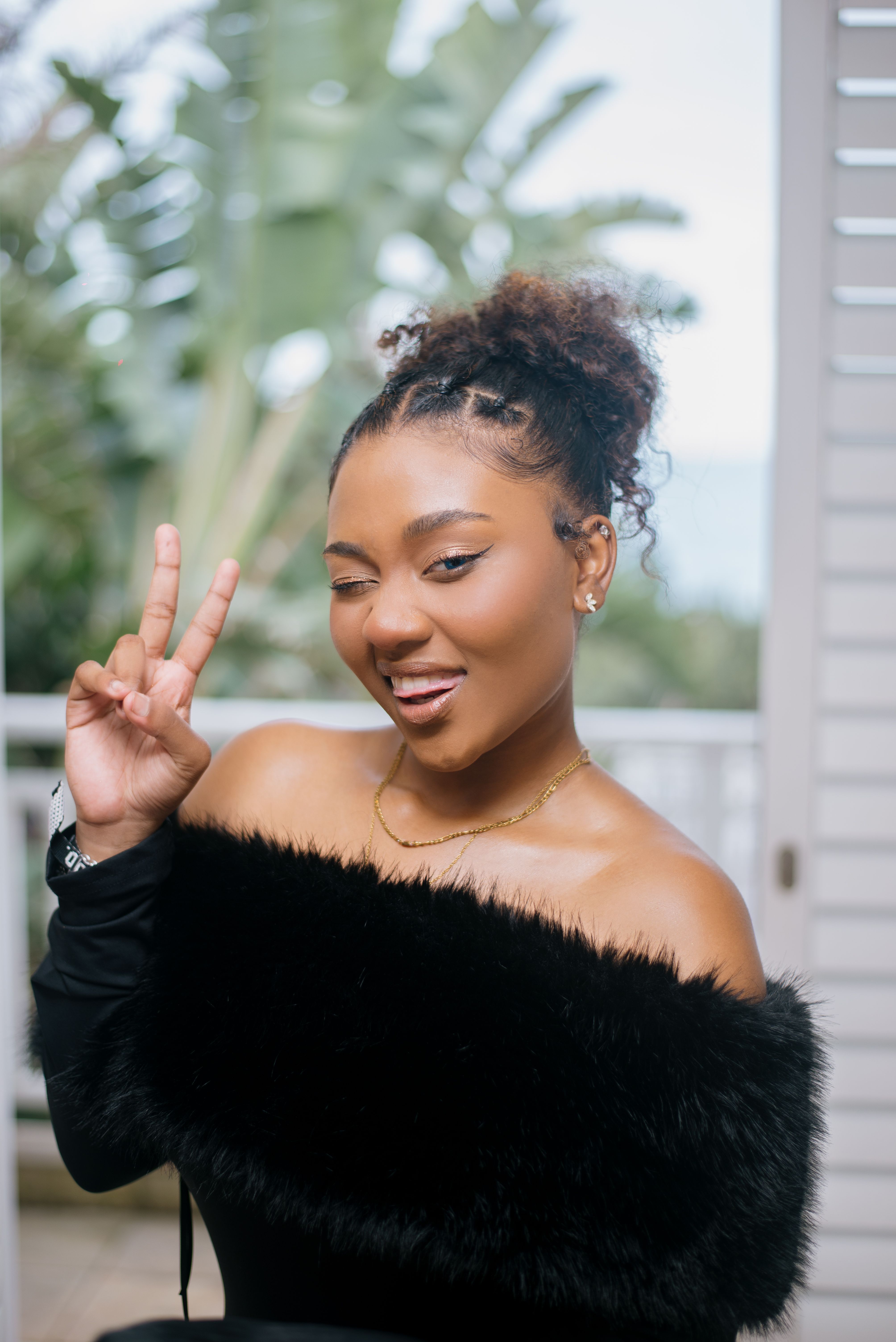 Young woman winking and making a peace sign with a playful expression outdoors.