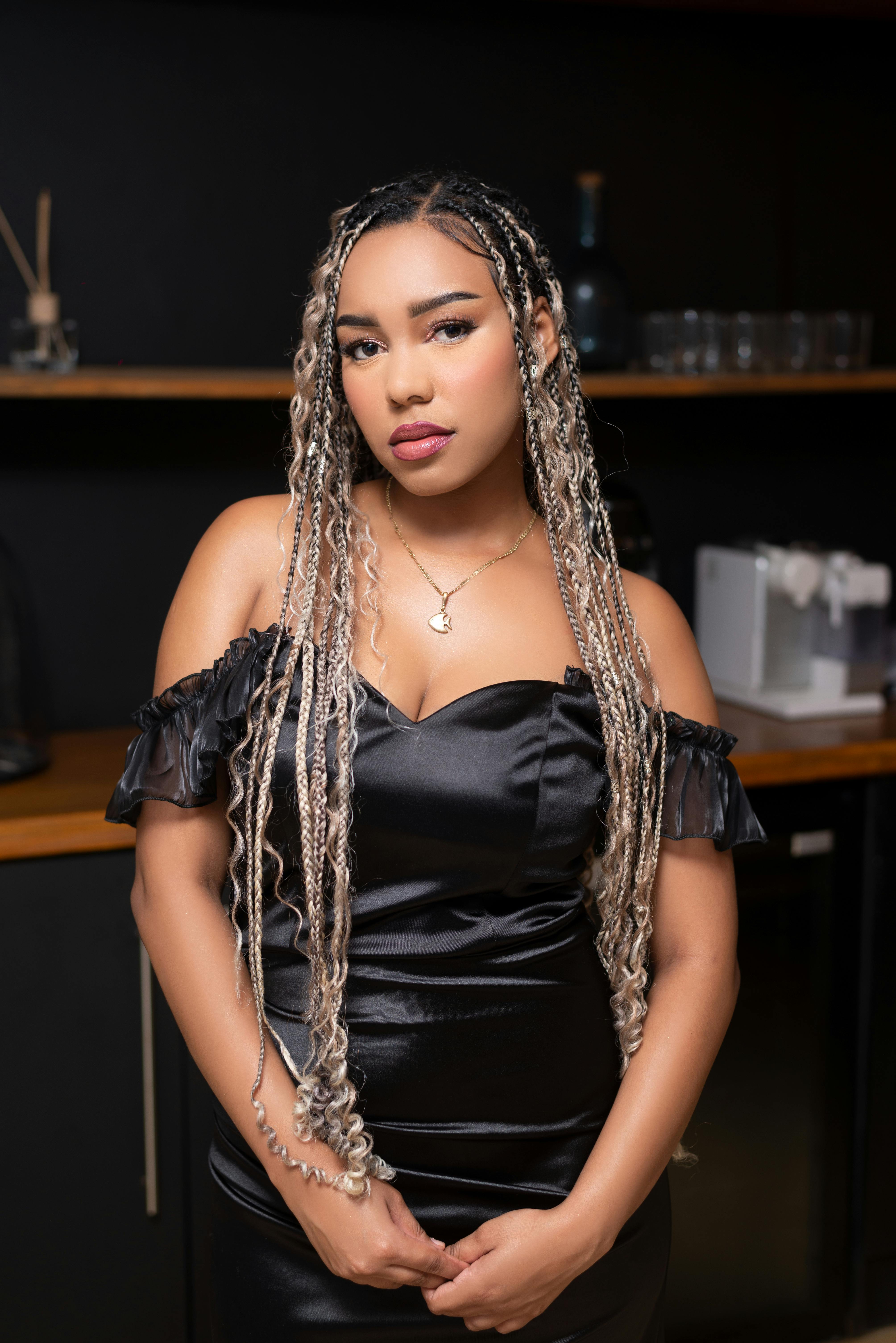 Elegant woman in black dress with braided hair posing indoors, modern style.