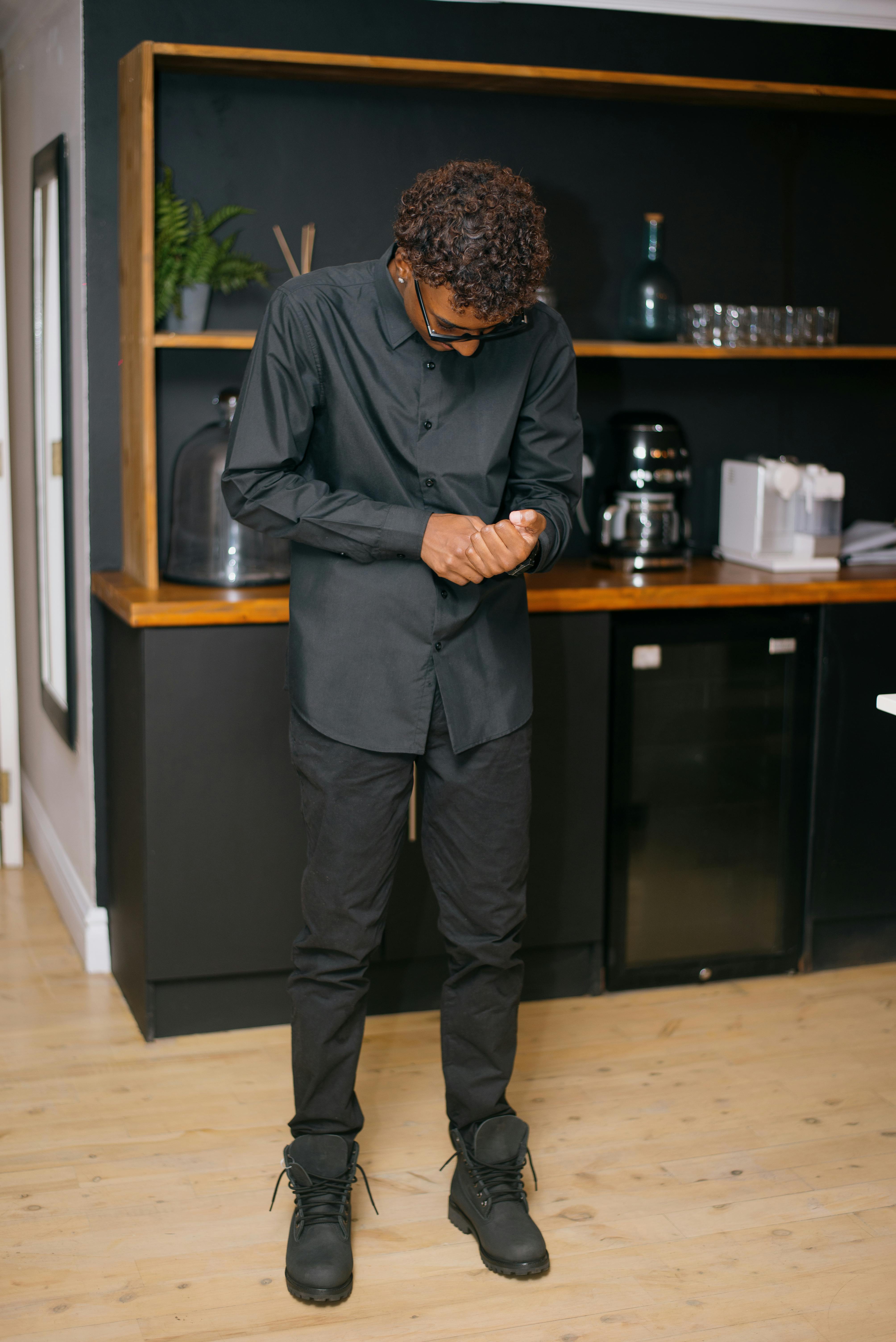 Free A young man buttoning his shirt while standing in a modern room. Stock Photo