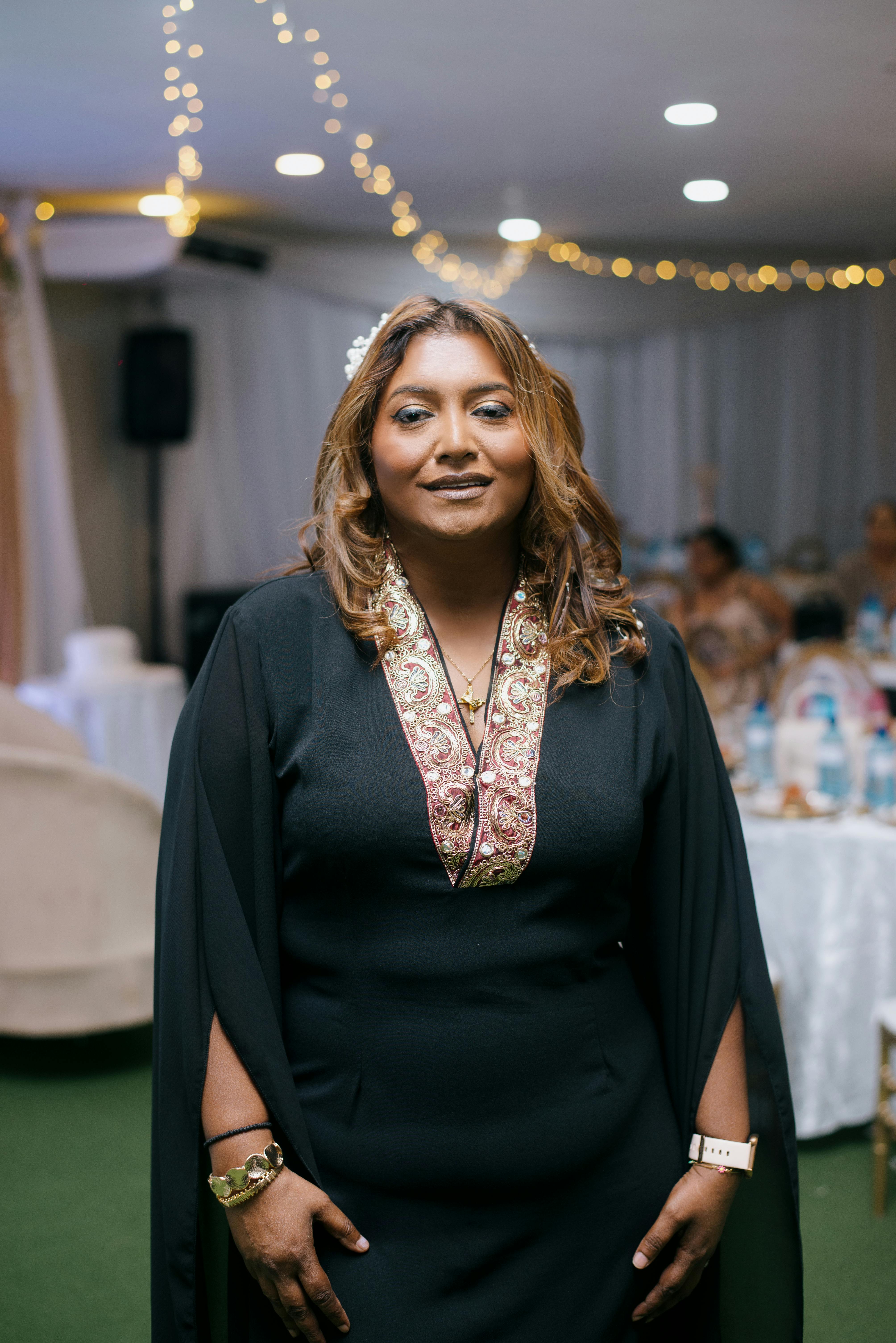 Miễn phí Người phụ nữ thanh lịch trong chiếc váy đen tạo dáng tại một buổi lễ trong nhà với ánh đèn rực rỡ. Ảnh lưu trữ