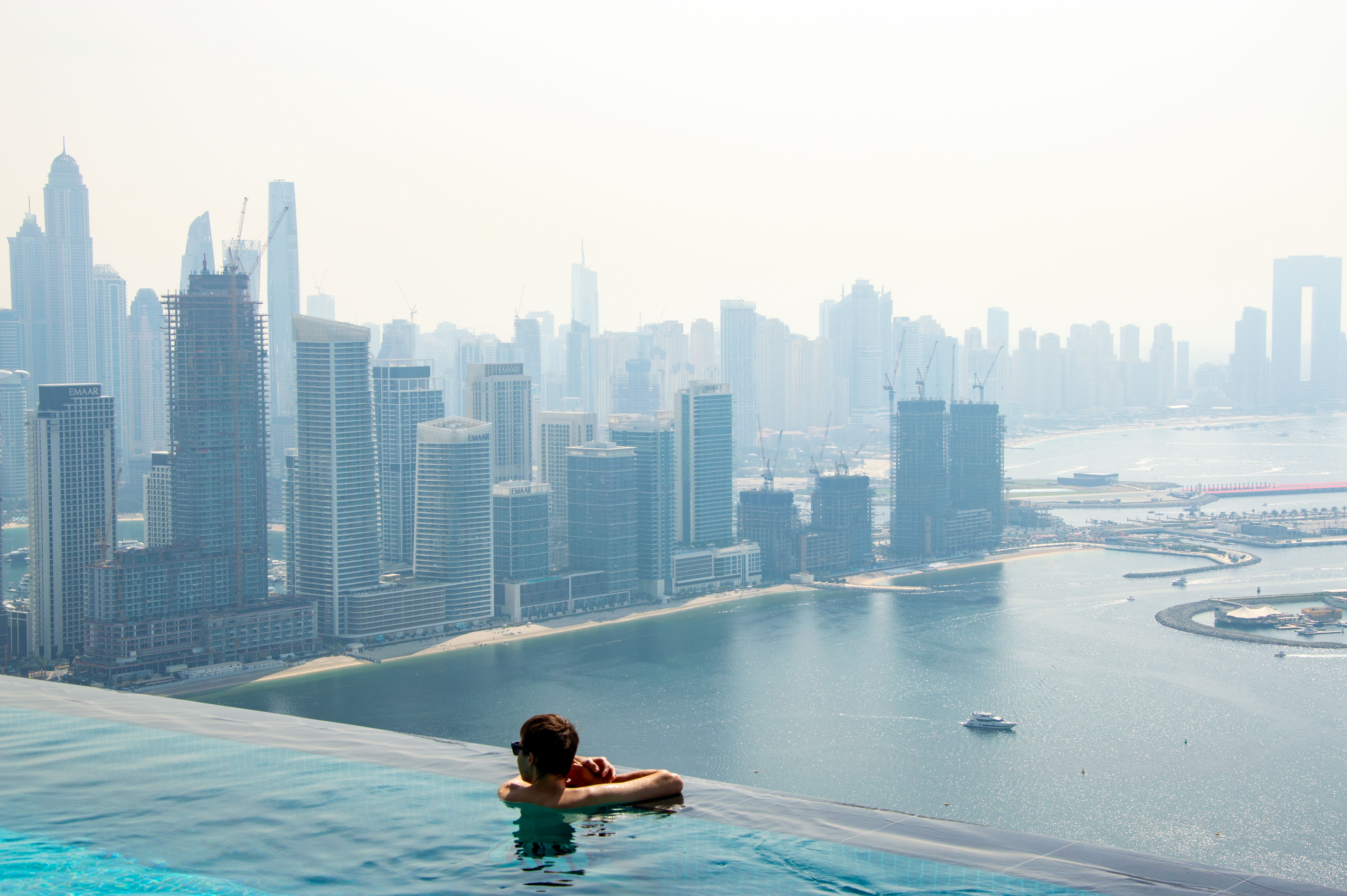 A person enjoys a rooftop pool with a stunning view of the Dubai skyline and waterfront.