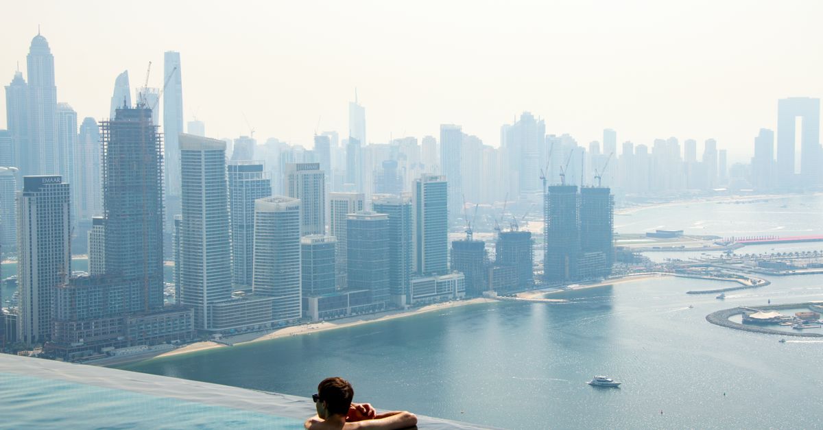 A person enjoys a rooftop pool with a stunning view of the Dubai skyline and waterfront.