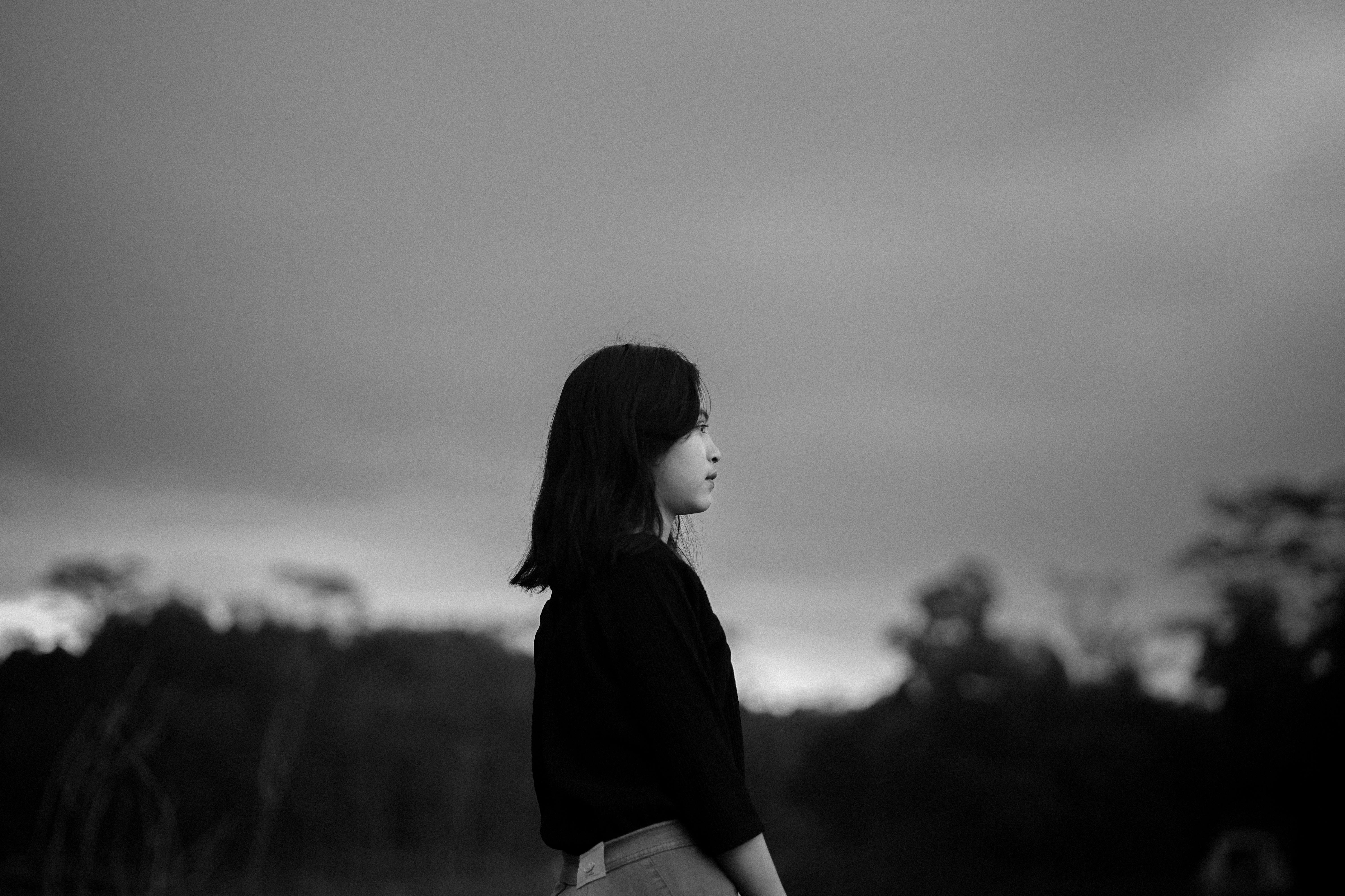 Gratis Un drammatico ritratto in bianco e nero di una donna che guarda lontano sotto un cielo nuvoloso. Foto a disposizione