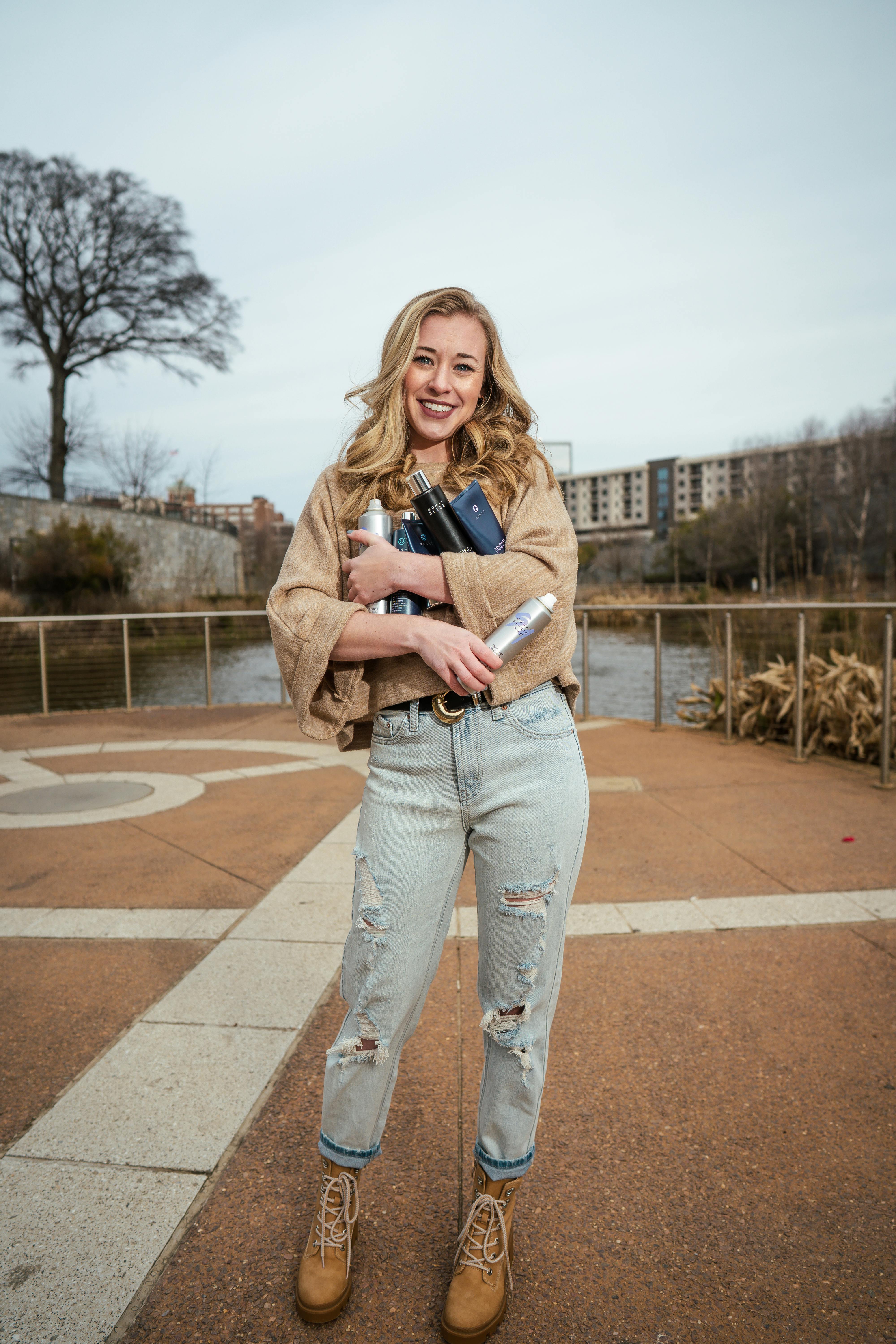 一位穿着休闲装、拿着书和水瓶的白人妇女，正站在人行道上微笑