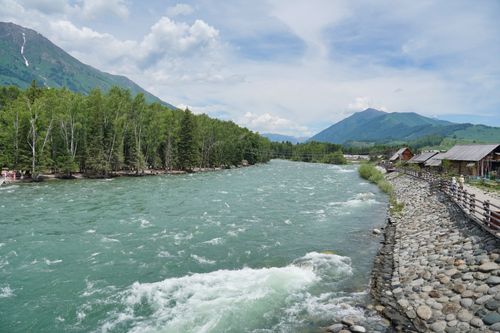 Free Vibrant river flowing through a picturesque mountain landscape with nearby village houses. Stock Photo