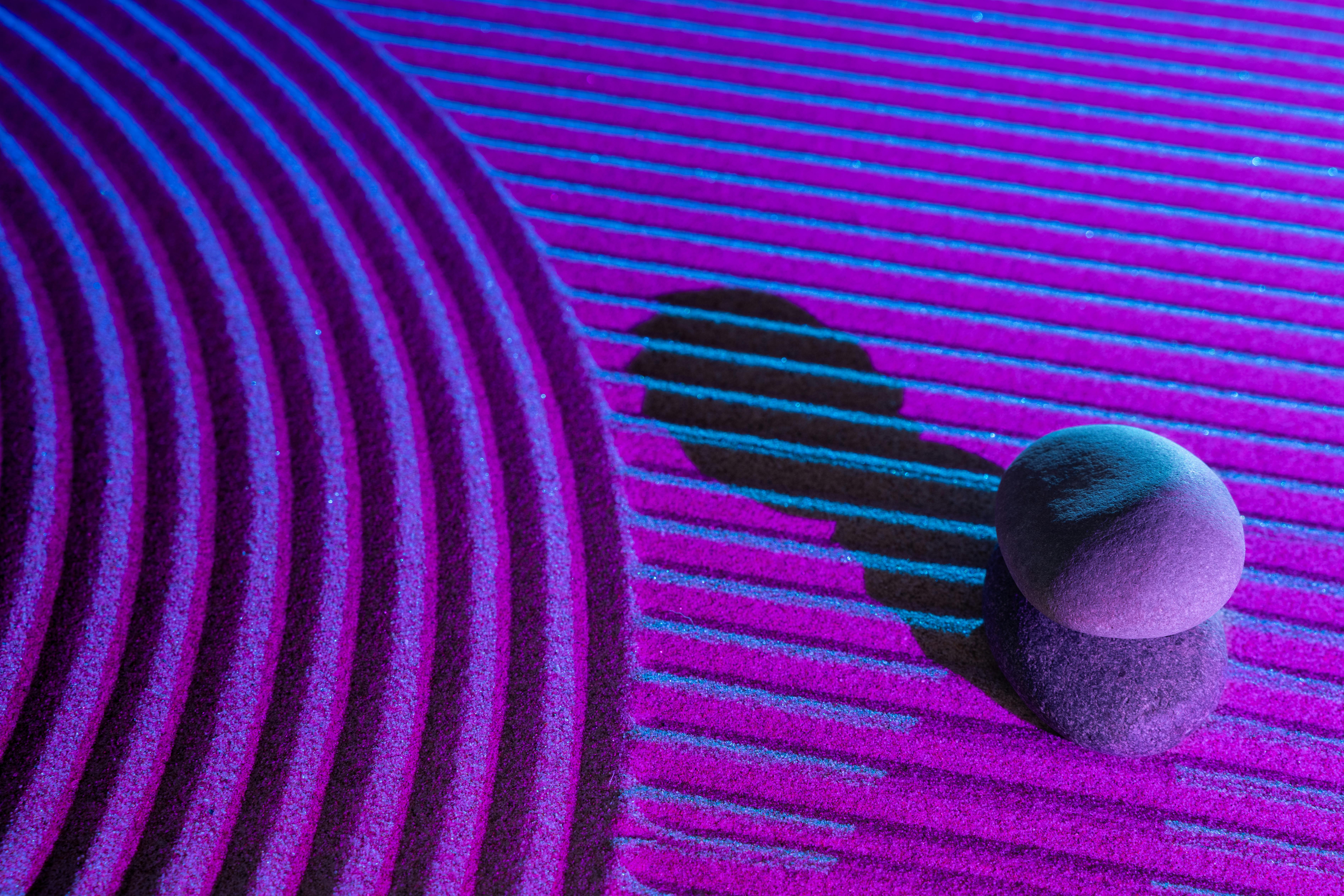 Gratis Pietre impilate proiettano ombre su una superficie vibrante e strutturata, illuminata da luci blu e rosa. Foto a disposizione