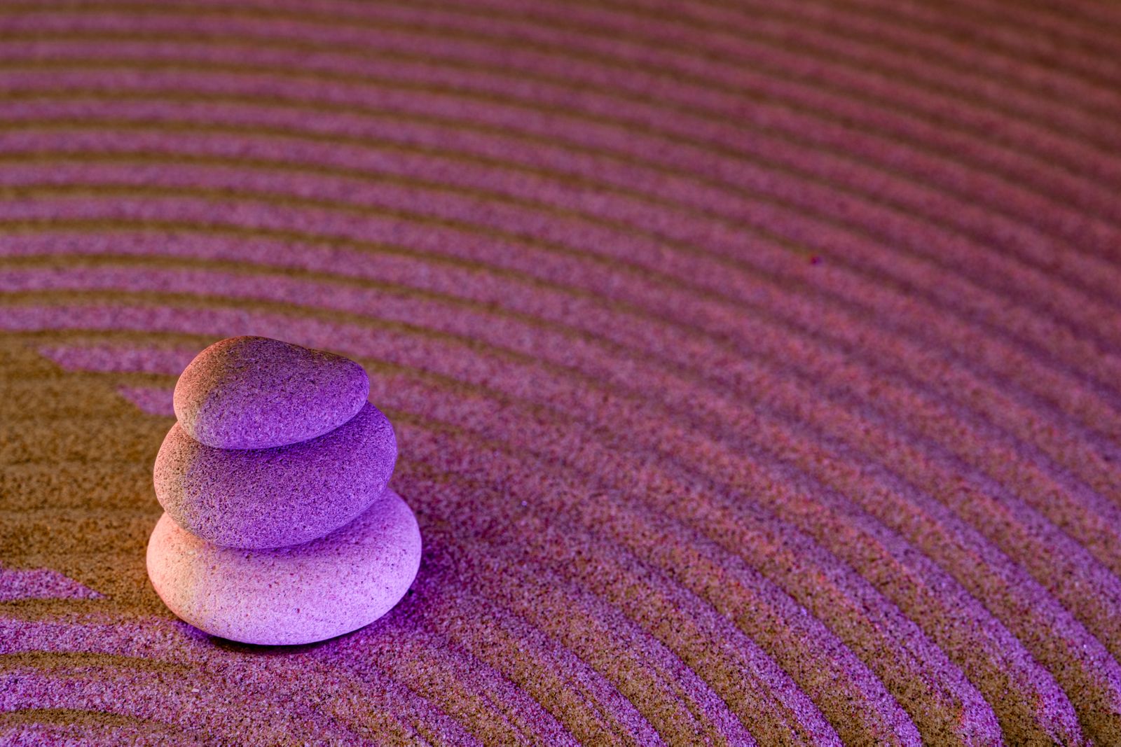 Serene zen garden with stacked stones on raked sand illuminated in purple light