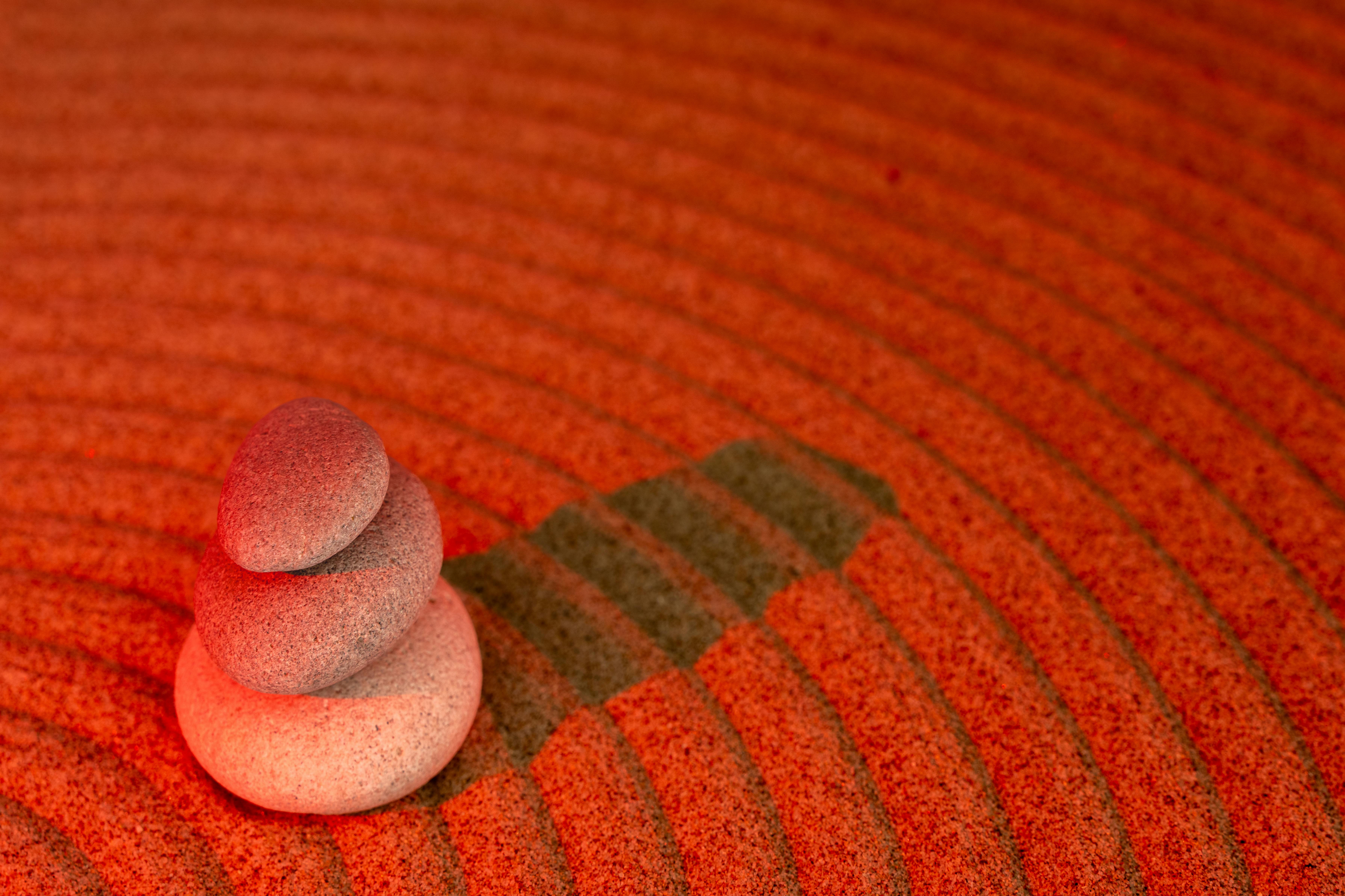 Serene arrangement of stacked stones in a red sand zen garden, symbolizing peace.