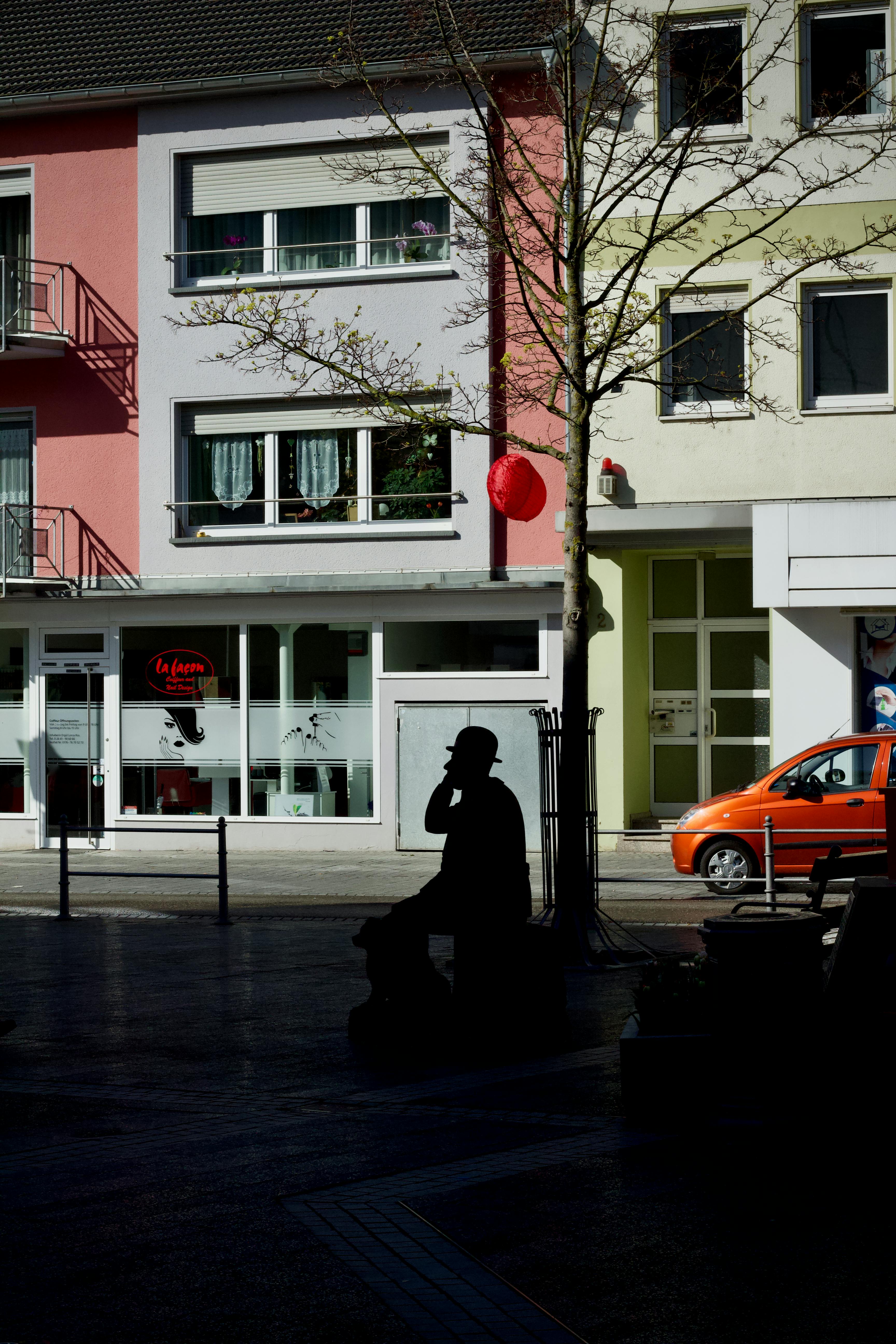 Gratis Silhouette di una persona seduta su una panchina in una colorata strada urbana con facciate di edifici vivaci. Foto a disposizione