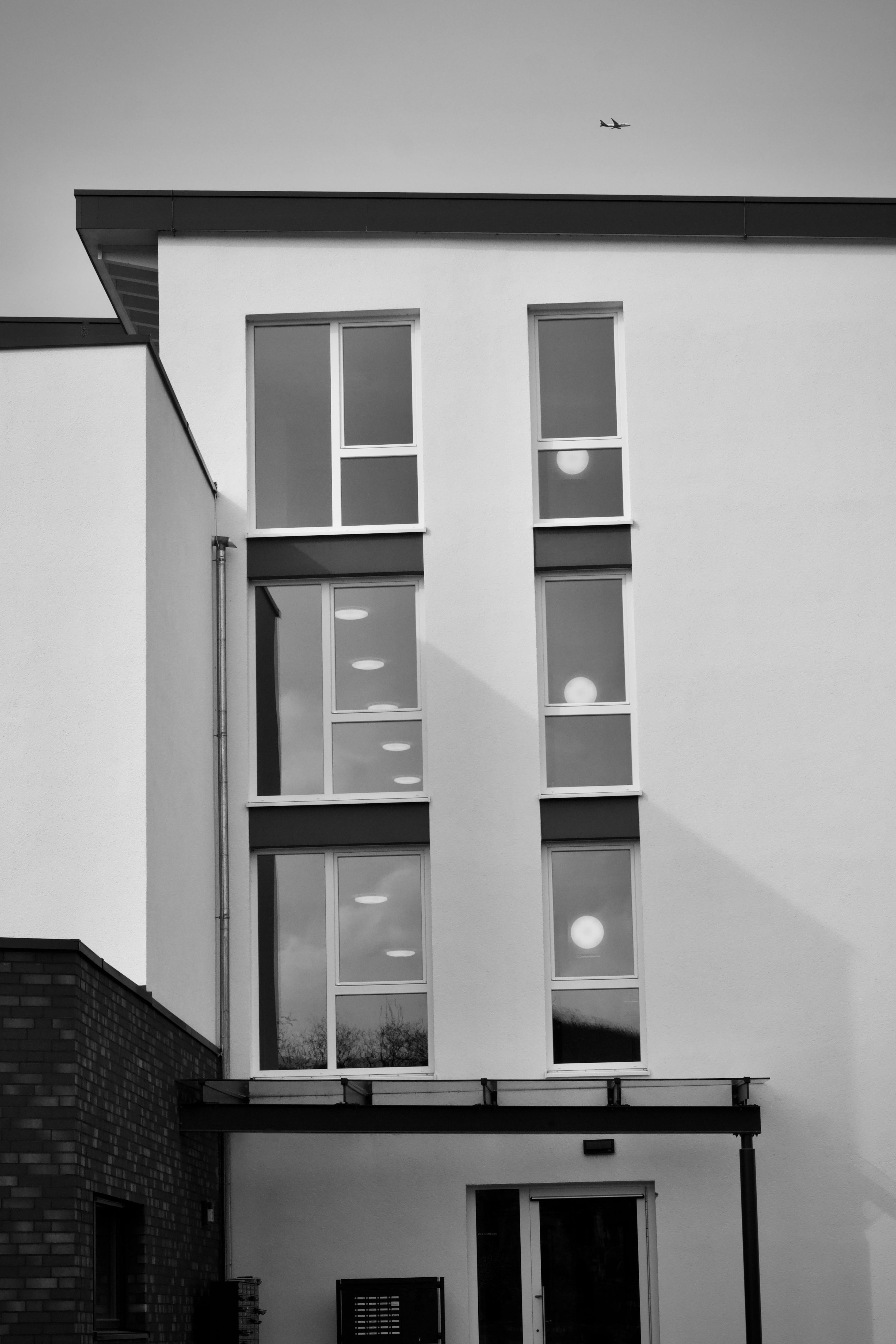 Kostnadsfria Svartvitt foto av en modern byggnadsfasad med flygplan i himlen. Stock foto