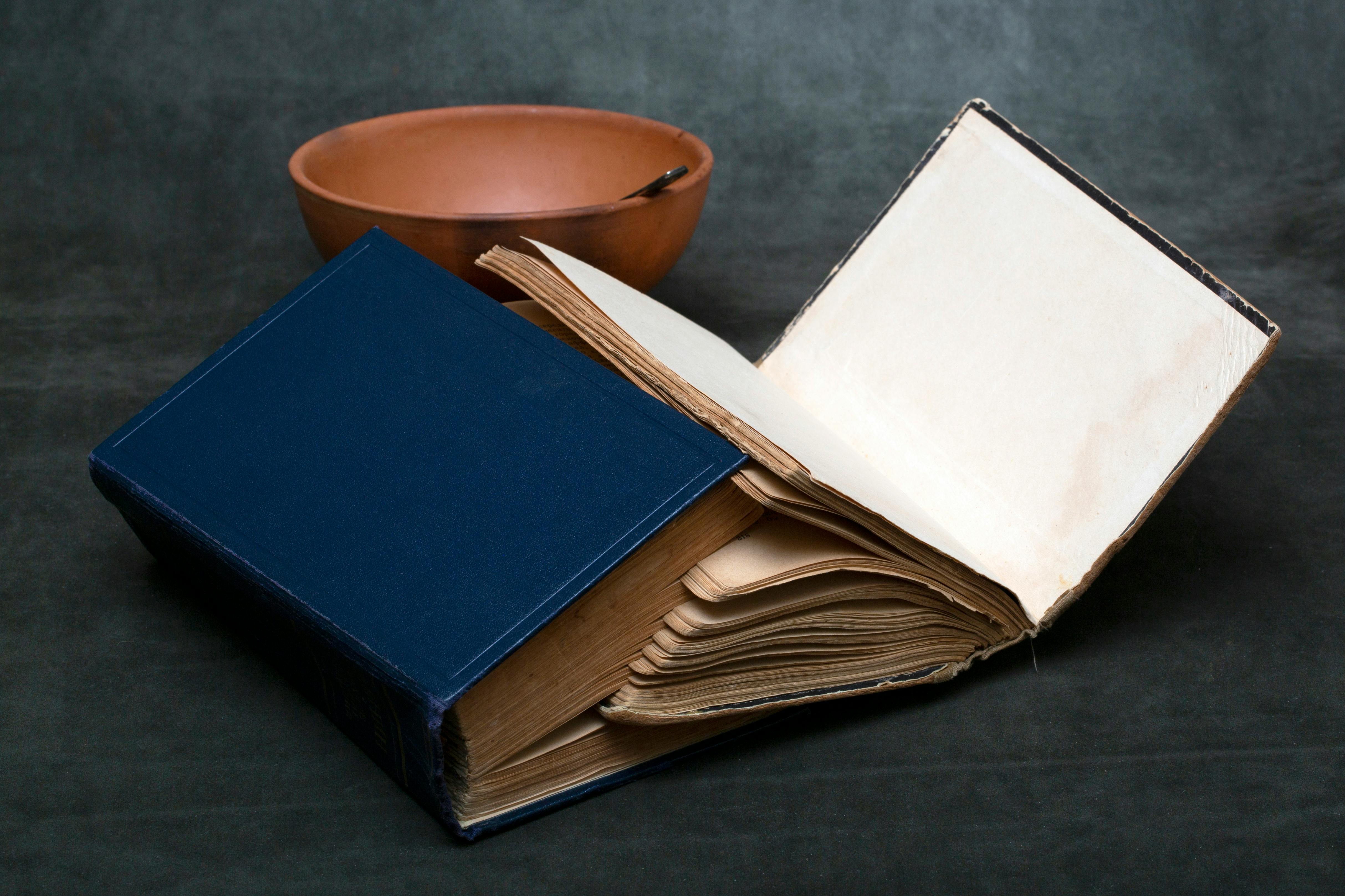 Ücretsiz Eski bir kitap, kil bir kasenin yanında açık durarak rustik ve entelektüel bir atmosfer yaratıyor. Stok Fotoğraflar